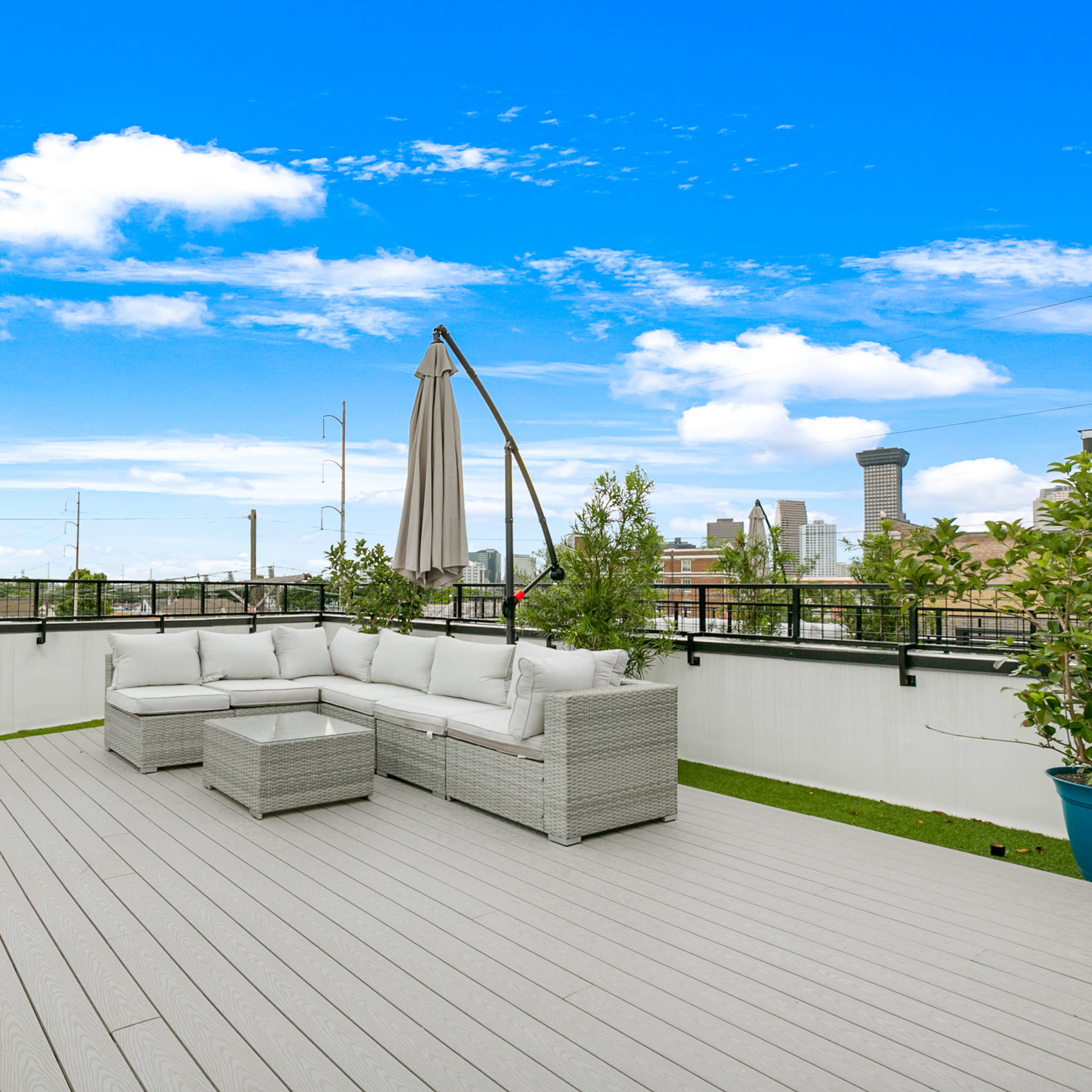 A rooftop deck with a seating area, umbrella, and city skyline in the background under a clear blue sky.