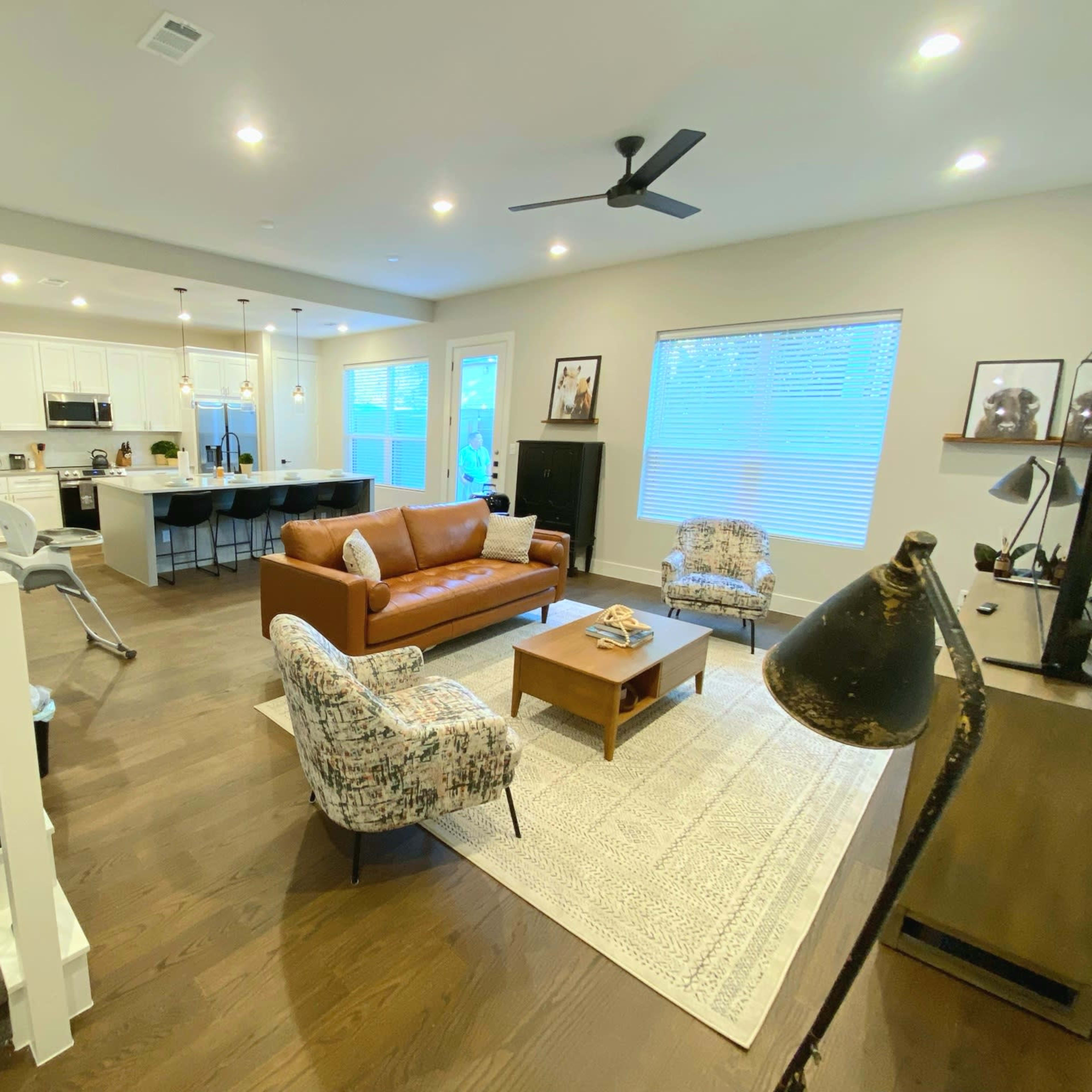 A modern living room with a brown leather sofa, two patterned chairs, a coffee table, and a staircase leading to an upper level.