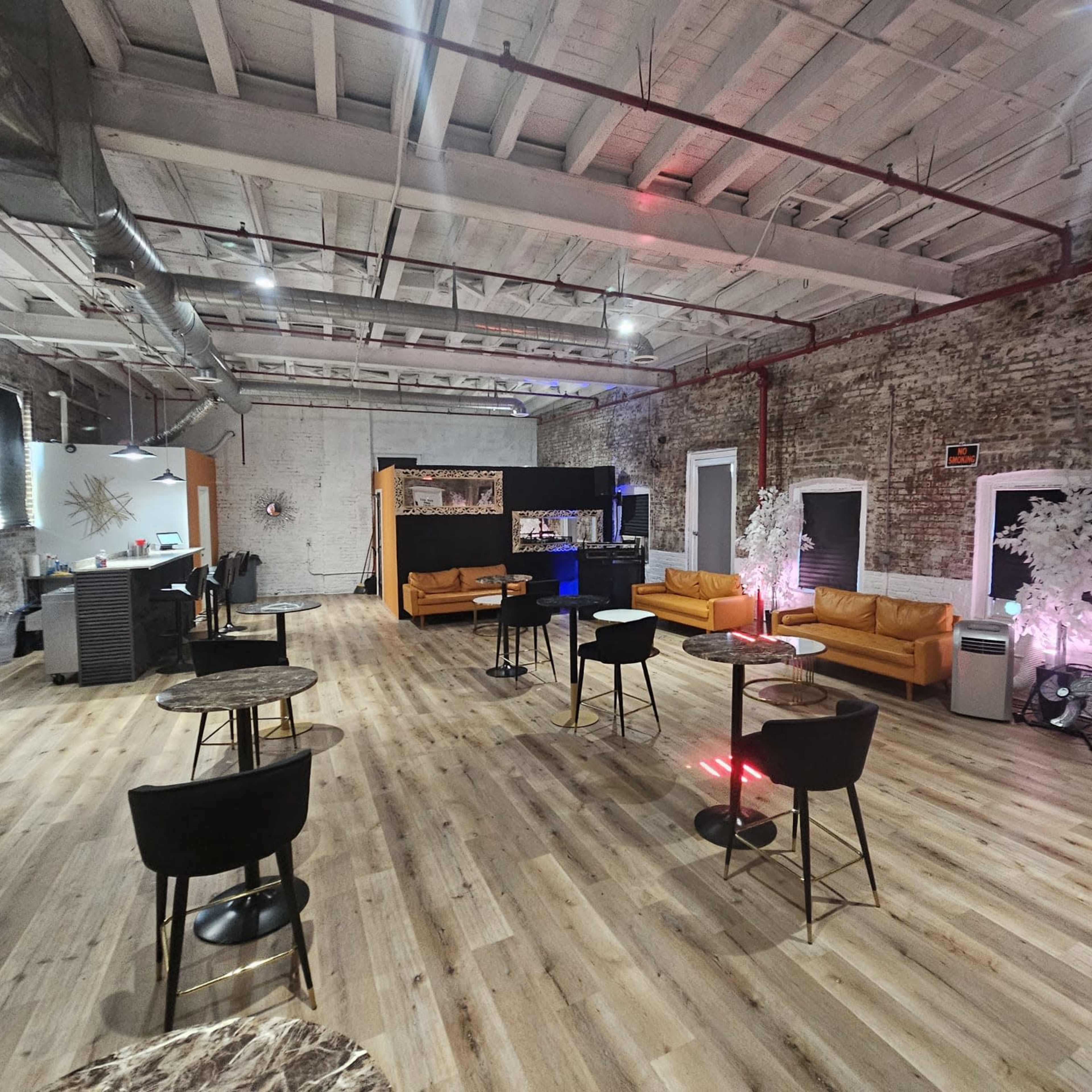 An industrial-style event space with exposed brick walls, wooden floors, and several seating areas featuring orange couches and small tables.