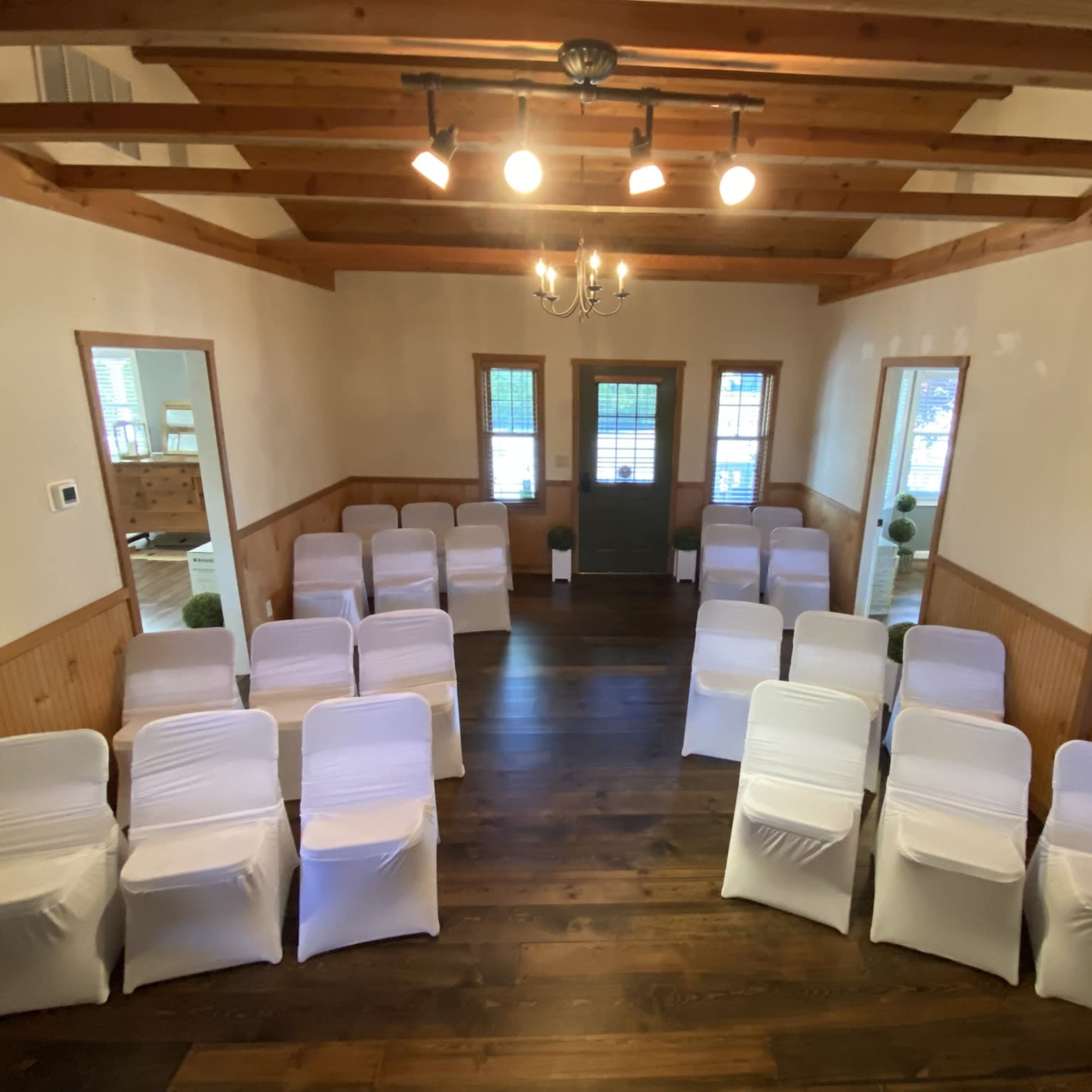 A room set up for an event with neatly arranged rows of white-covered chairs facing a green door.