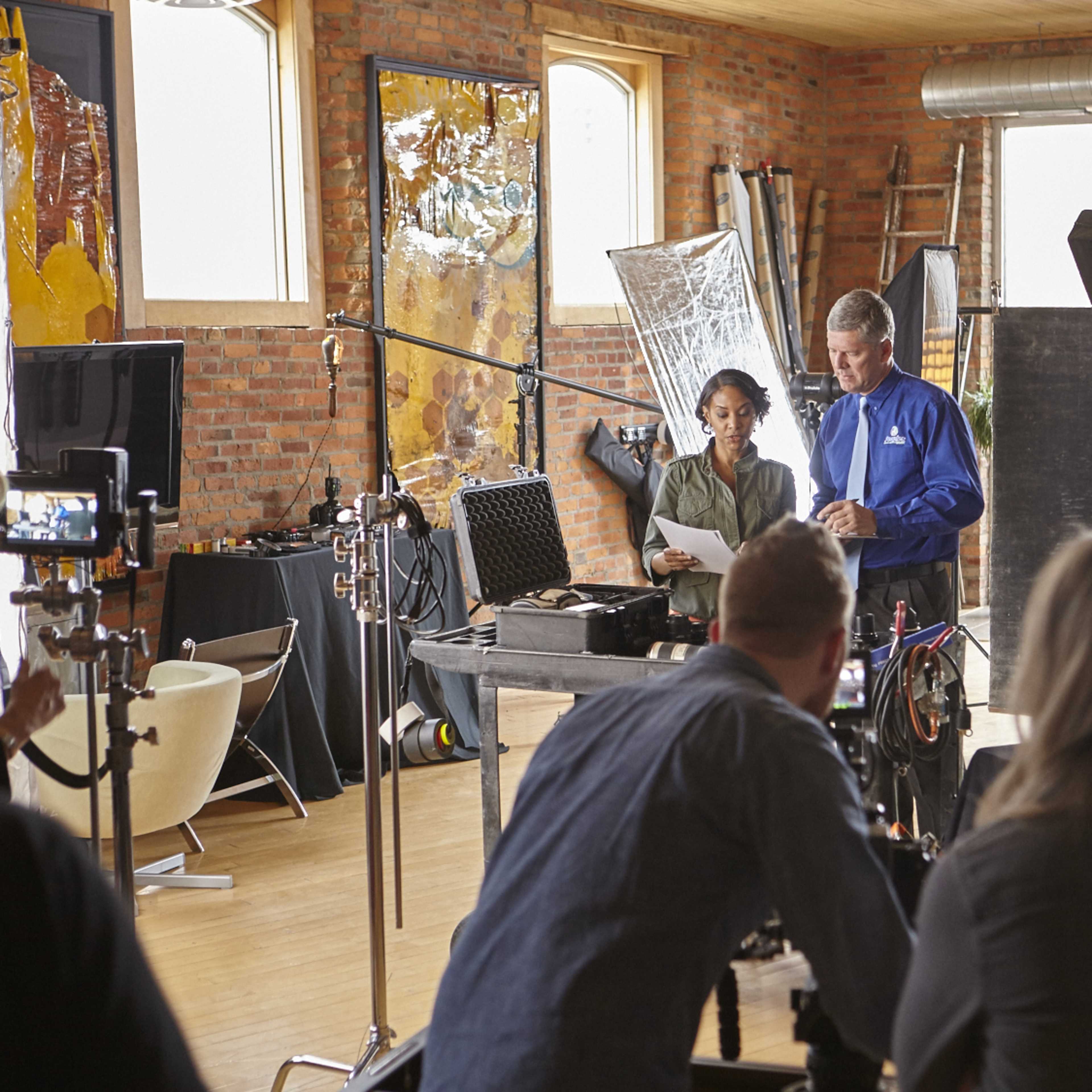 A group of people works in a photography studio, setting up equipment and reviewing shots on a computer.
