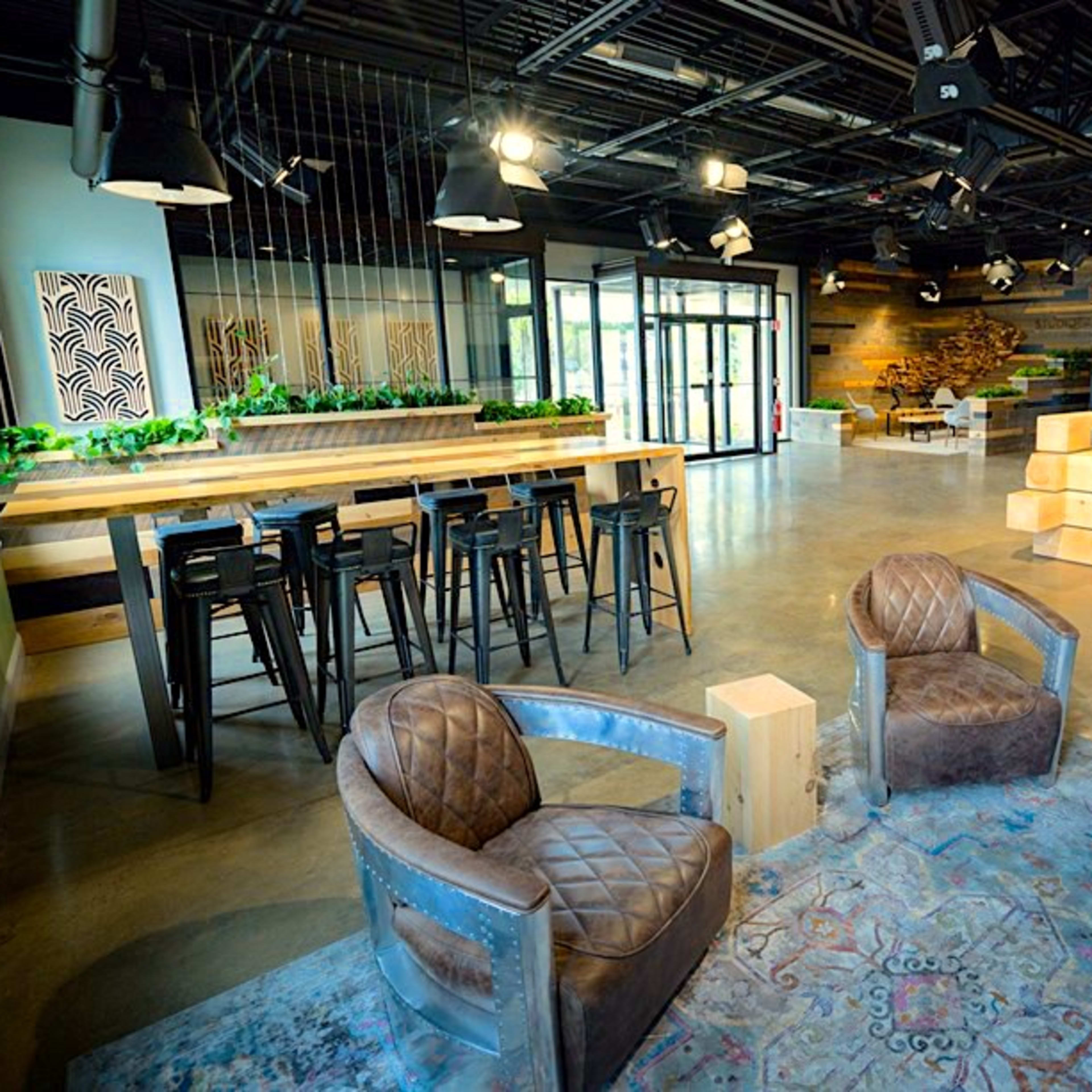 A modern open space with a seating area, bar-style tables, and decorative plants.