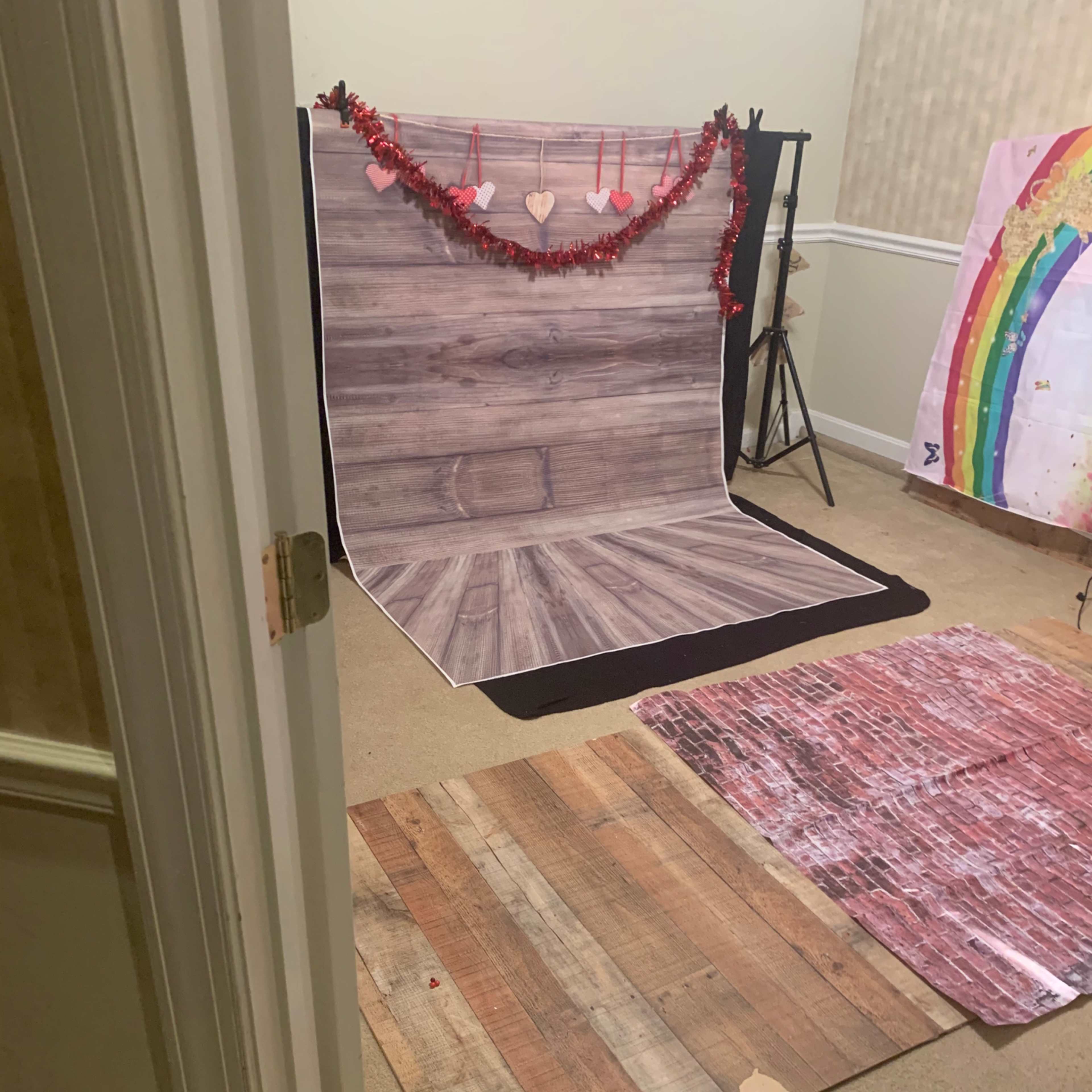 A photography setup with a wooden backdrop, decorative hearts, and various floor mats in a carpeted room.