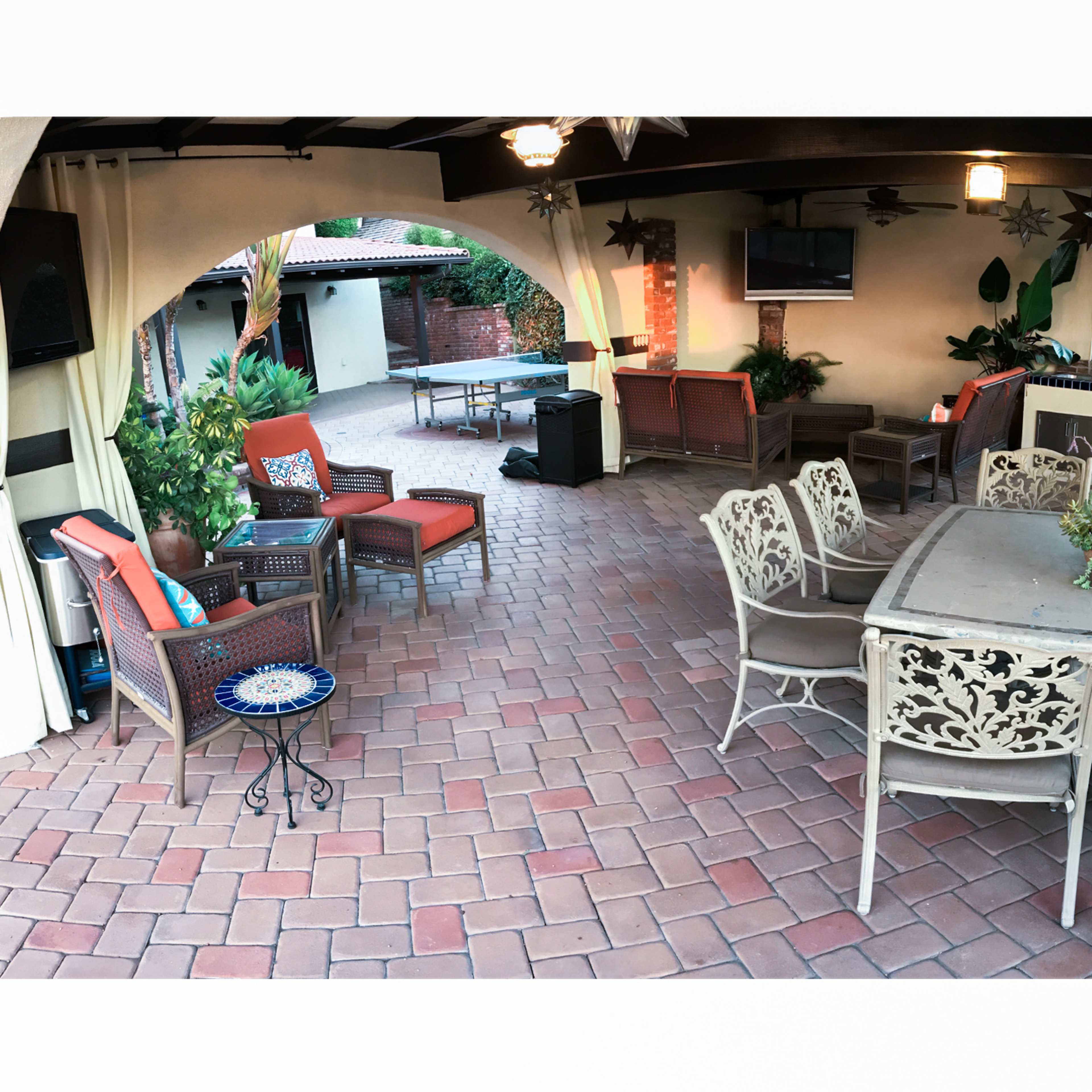 A patio area with a dining table, several chairs, a barbecuing station, and decorative plants.