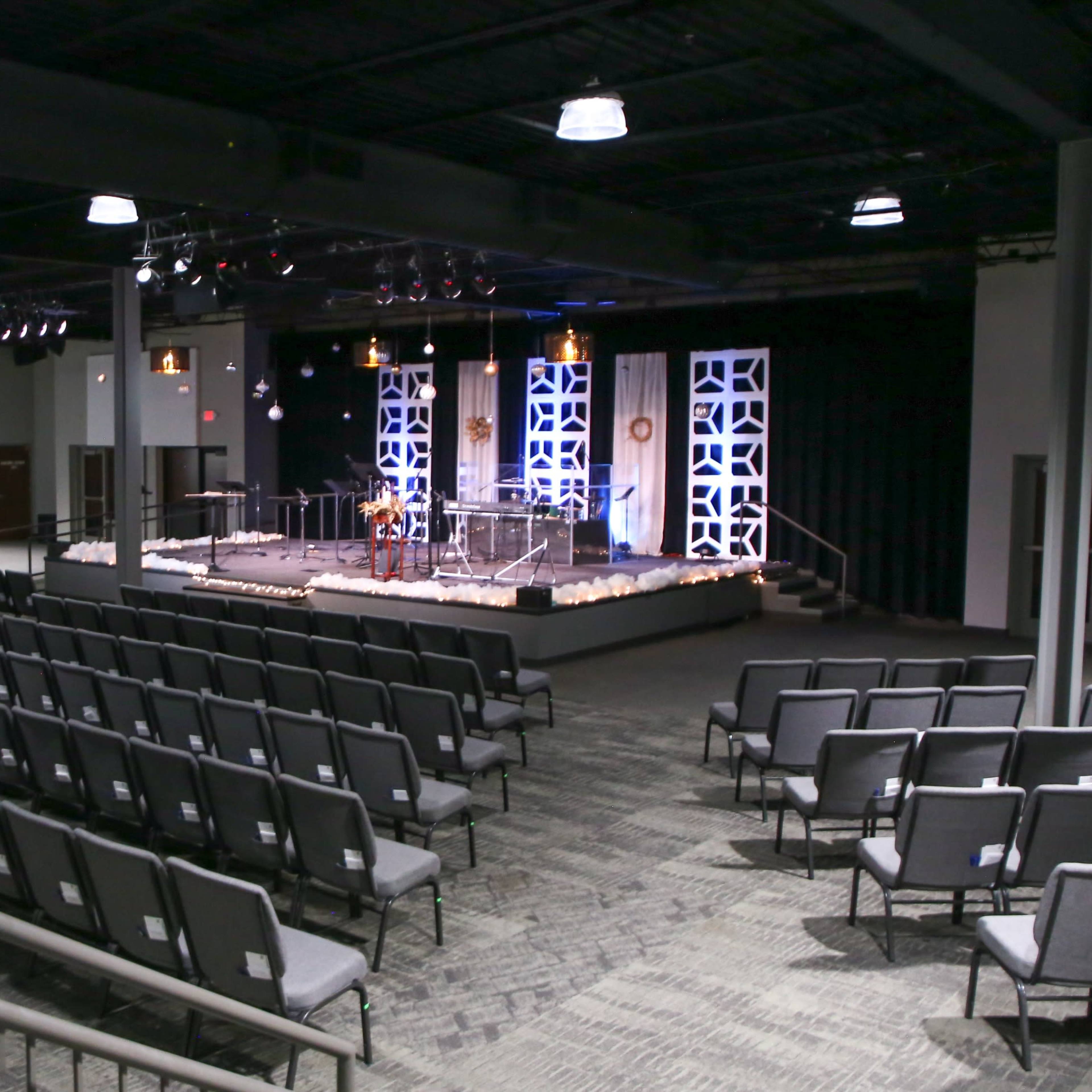 An empty auditorium with rows of chairs facing a stage equipped with lighting and decorative elements.