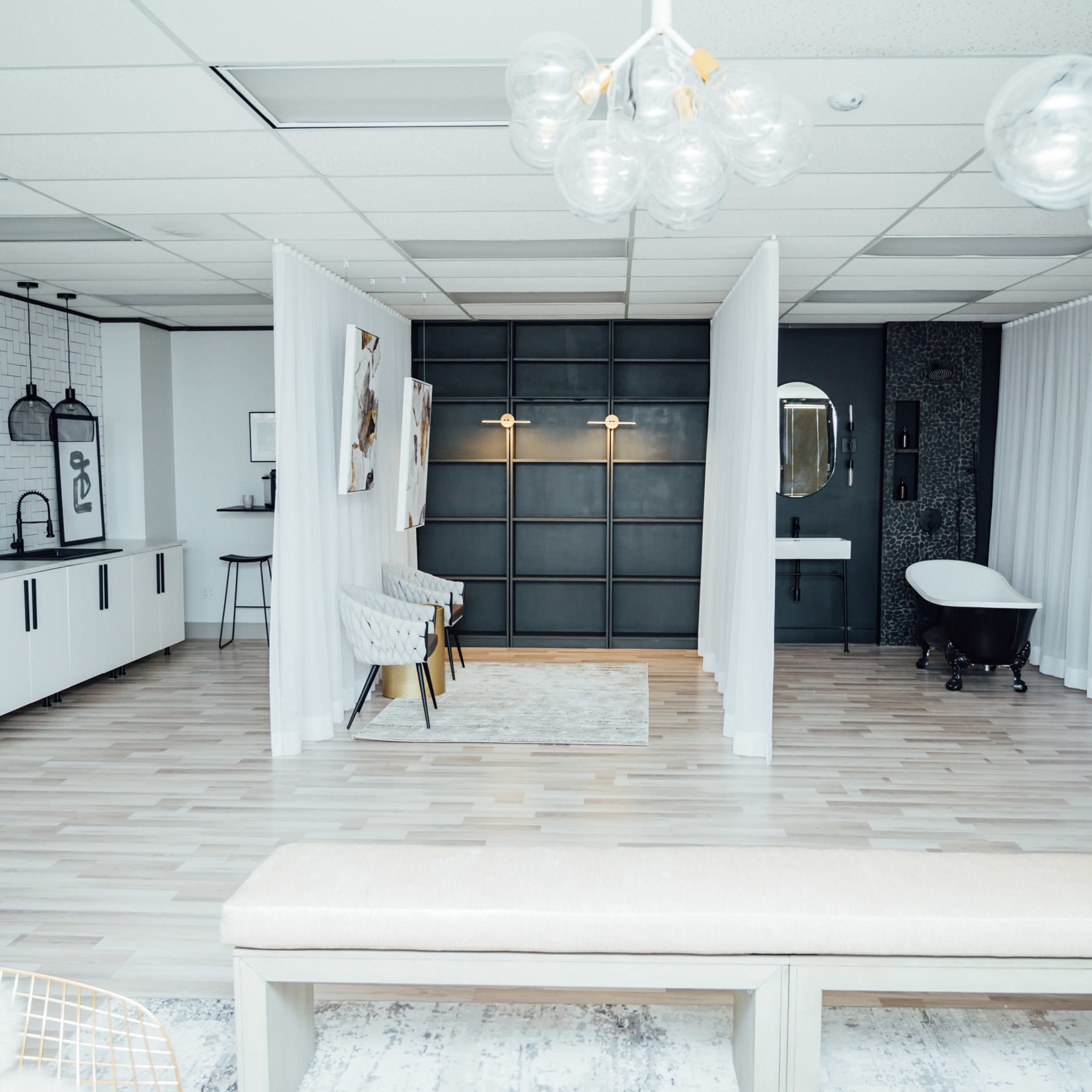 A modern, open space featuring a white and gray color palette, with separated areas defined by curtain partitions and a freestanding bathtub in the background.