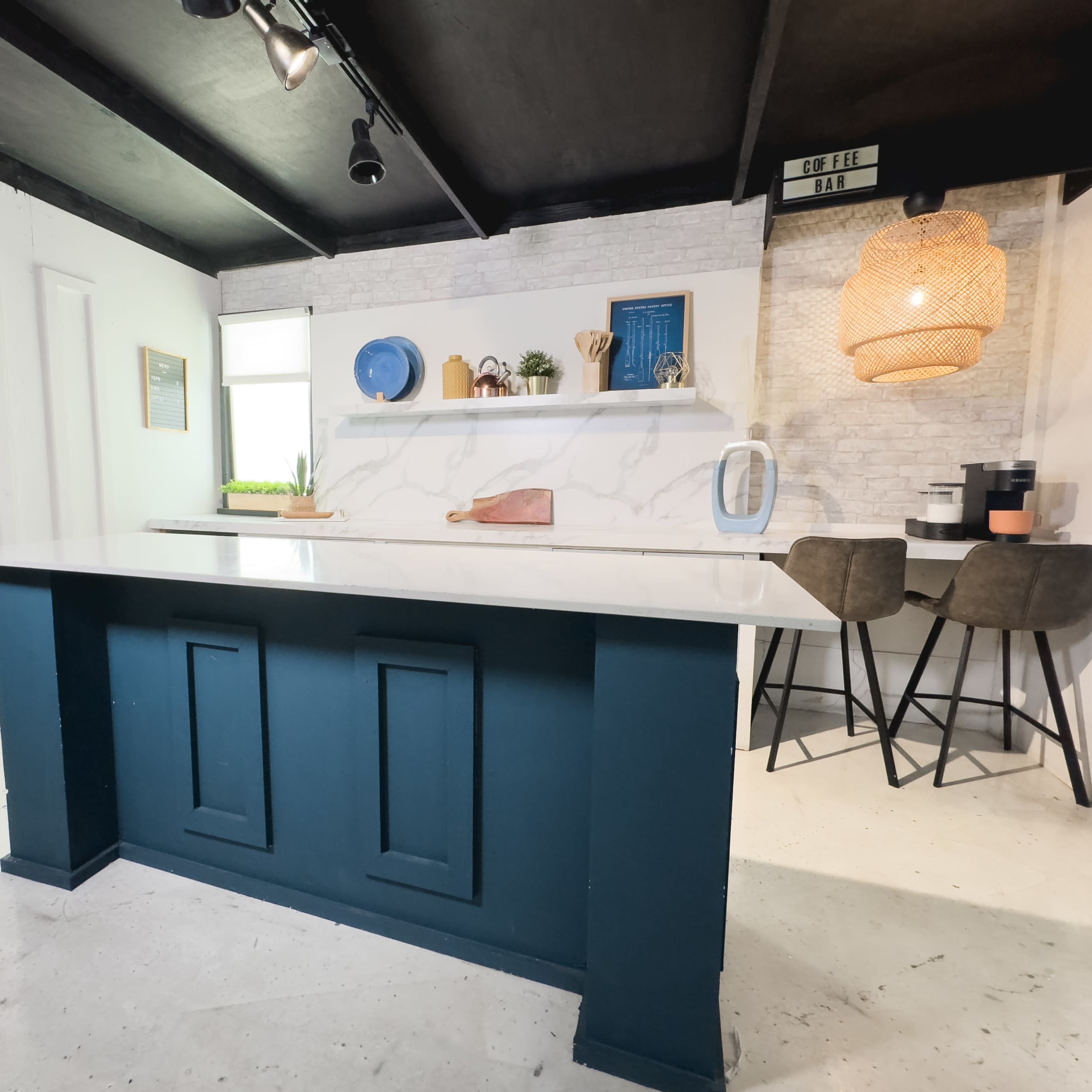 A modern kitchen with a blue island counter, a white brick wall, and a cozy dining area featuring two chairs and decorative items on shelves.