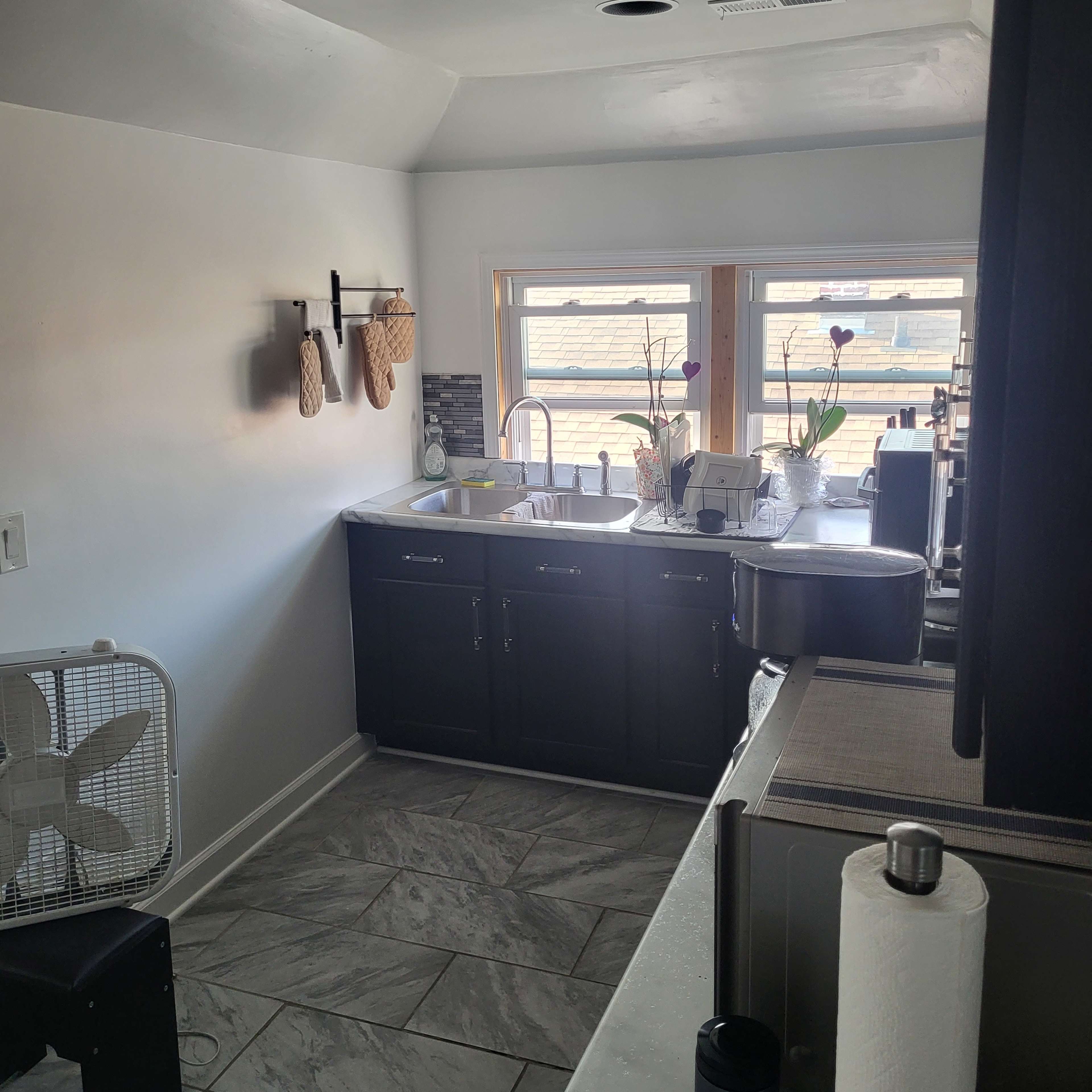 A small kitchen features dark cabinets, a double sink, and a countertop with a view of the outdoors through two windows.