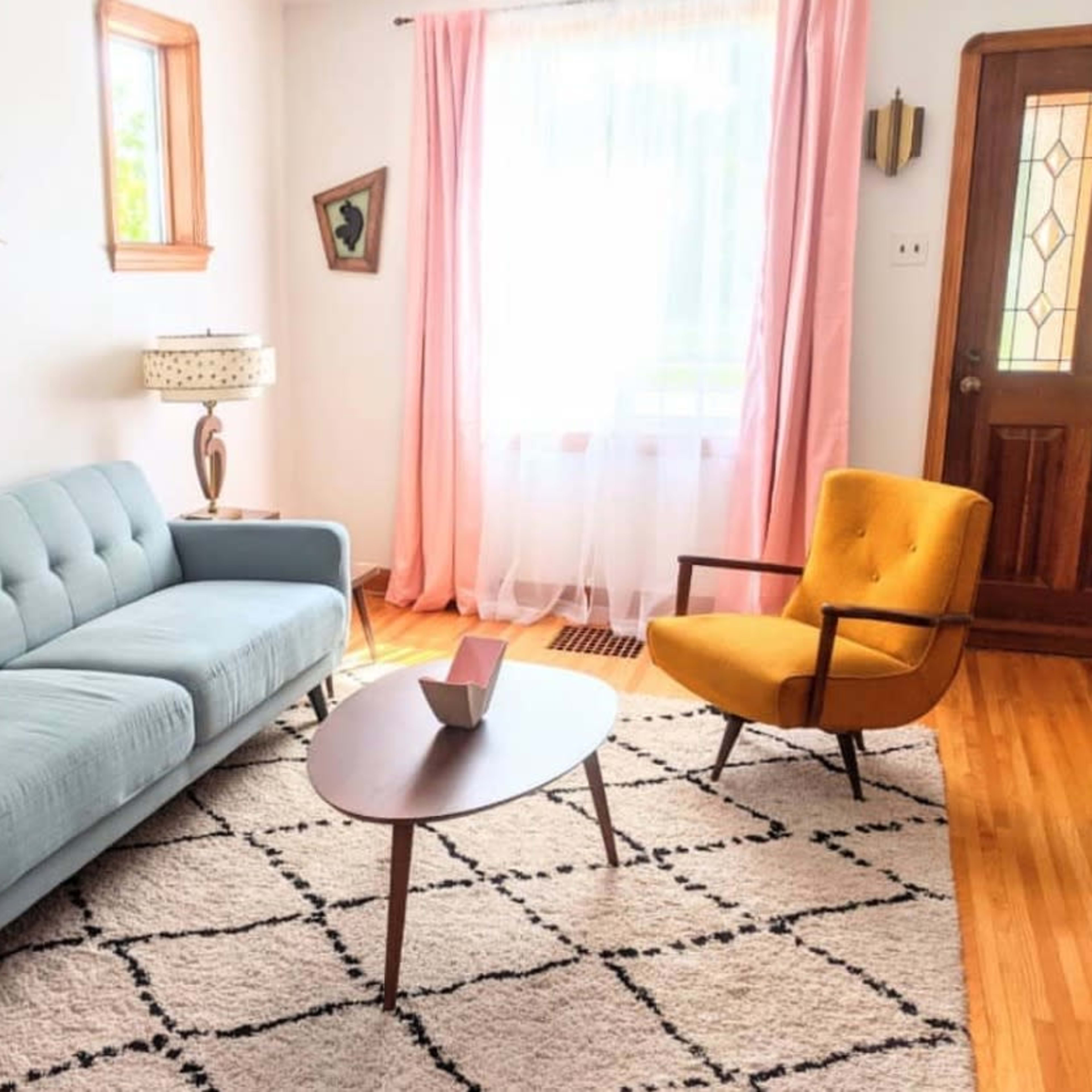 The living room features a light blue couch, a yellow armchair, a round coffee table, and large windows with sheer curtains.