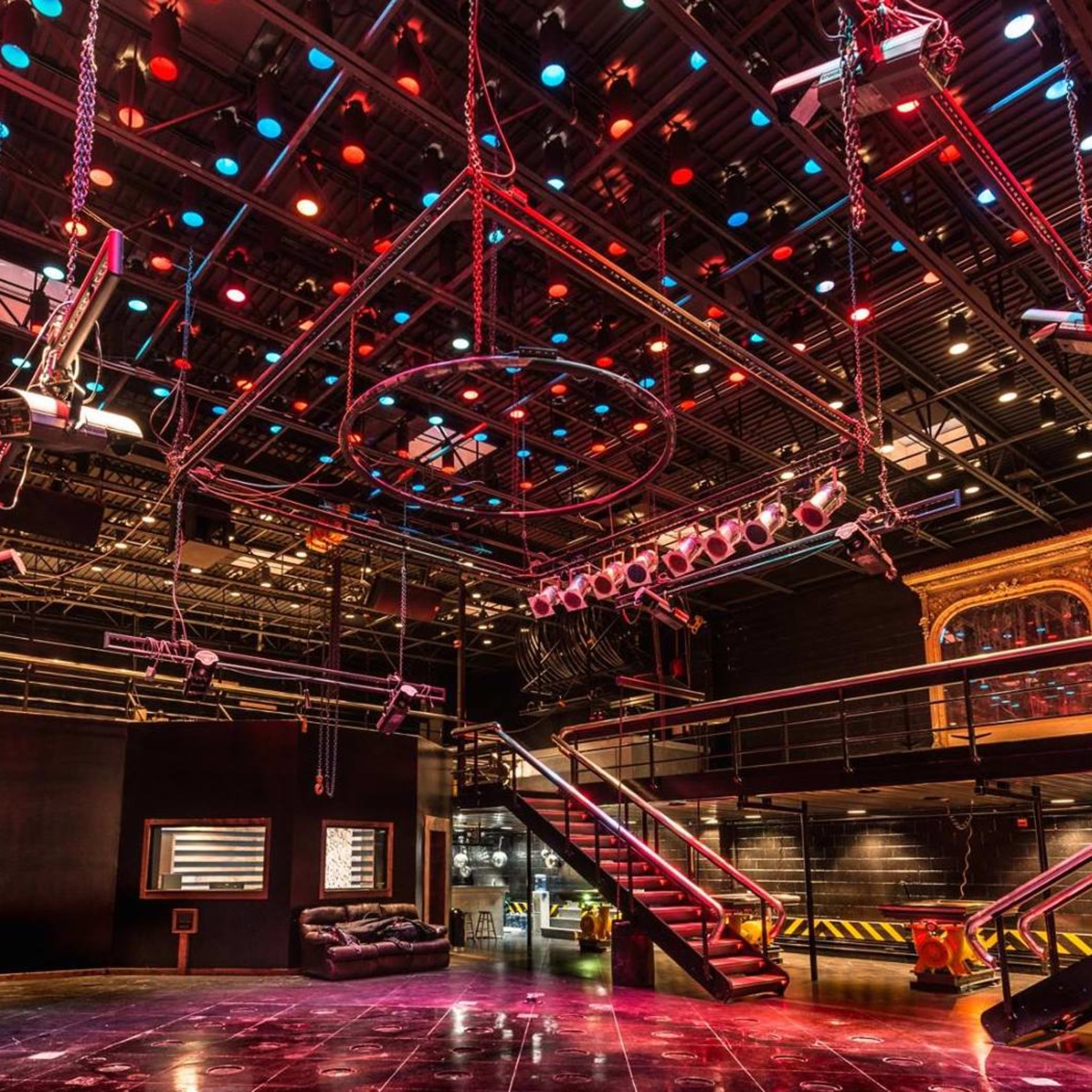 A large, empty performance space featuring a grid of overhead lights and a multi-level seating area with a glossy floor.