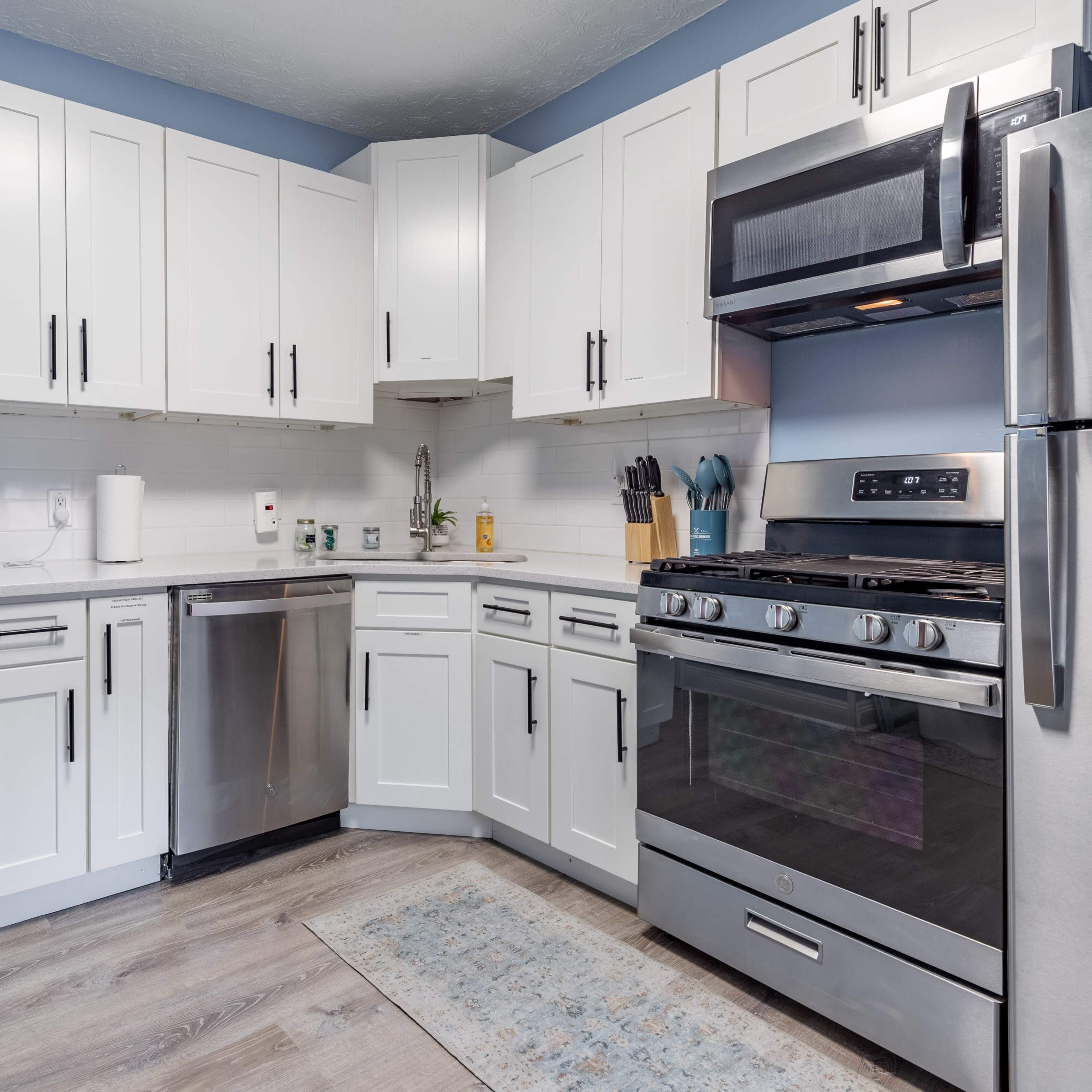 A modern kitchen features white cabinetry, stainless steel appliances, and a light-colored floor with a rug.