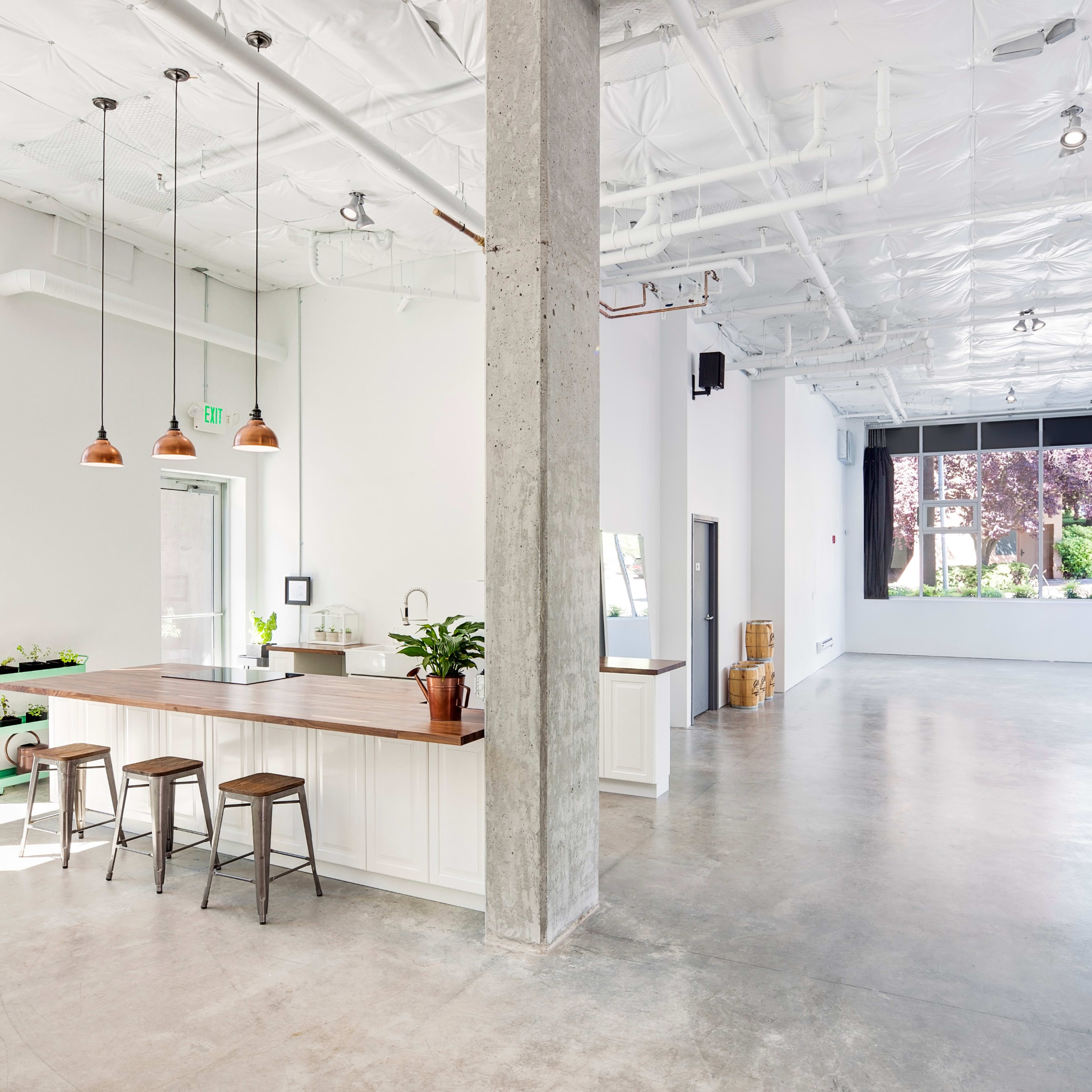 A spacious, well-lit room with a kitchen island, three bar stools, and large windows overlooking greenery.