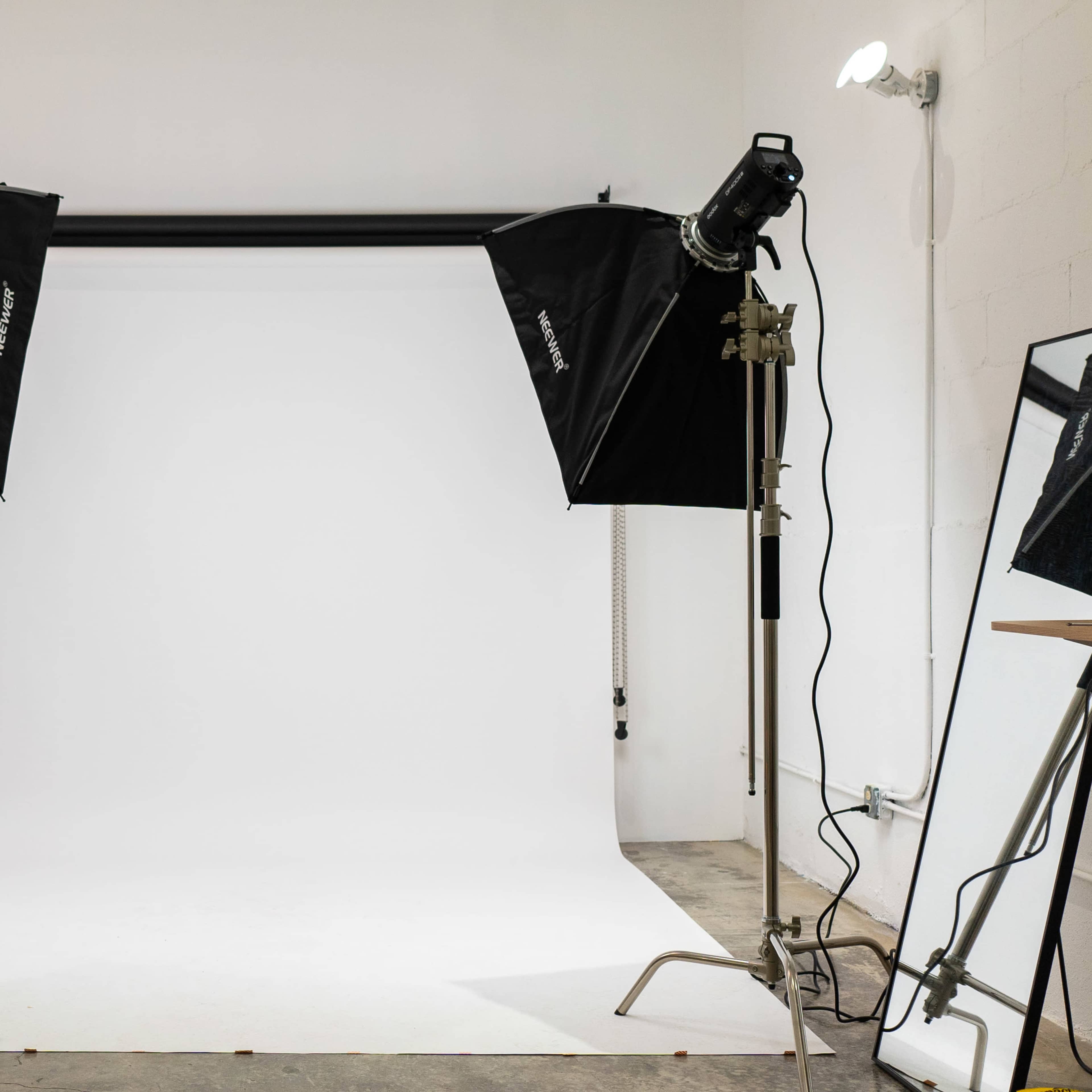 A photography studio setup with two light stands positioned on either side of a blank white backdrop.