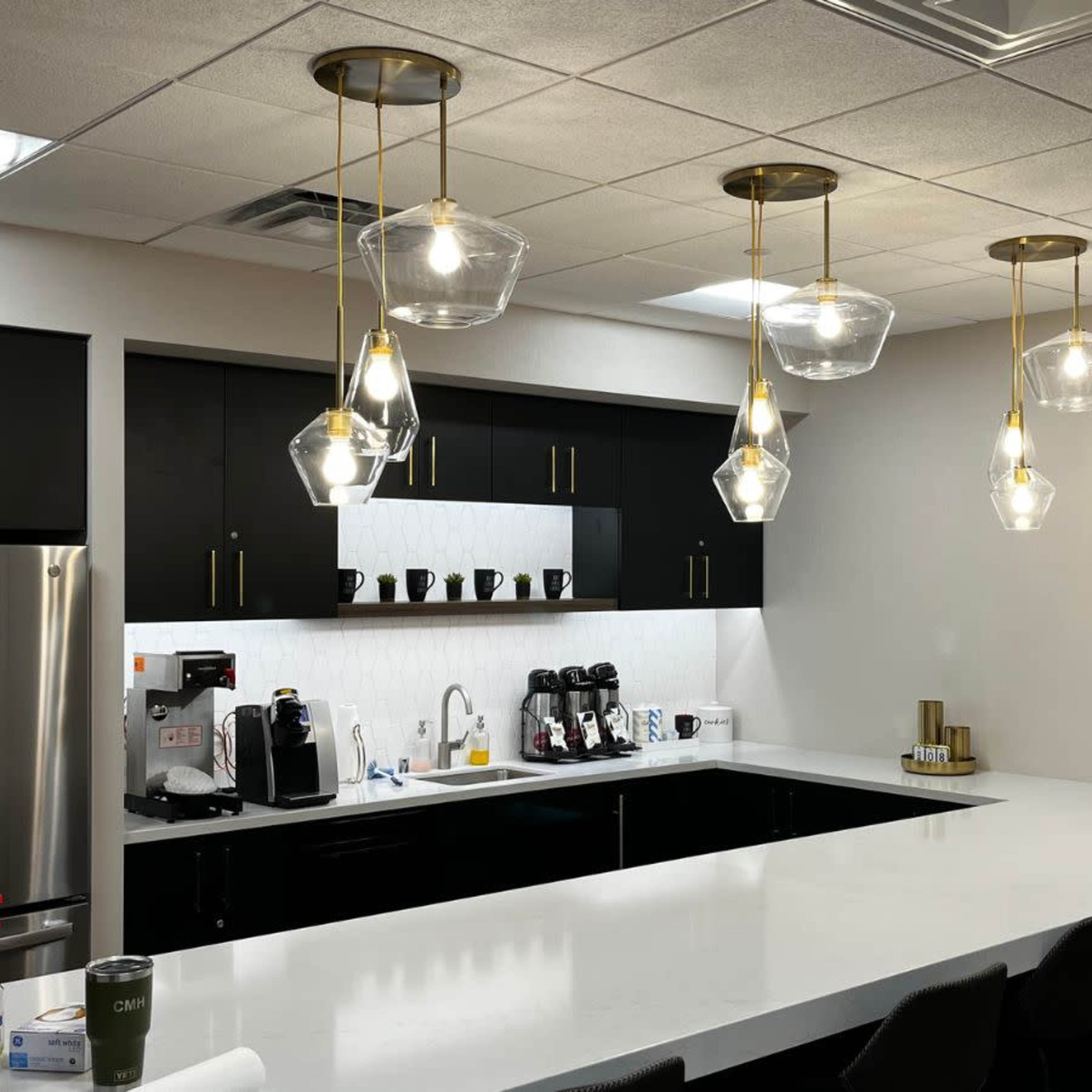 A modern kitchen with black cabinets, a long white countertop, stainless steel appliances, and pendant lighting.