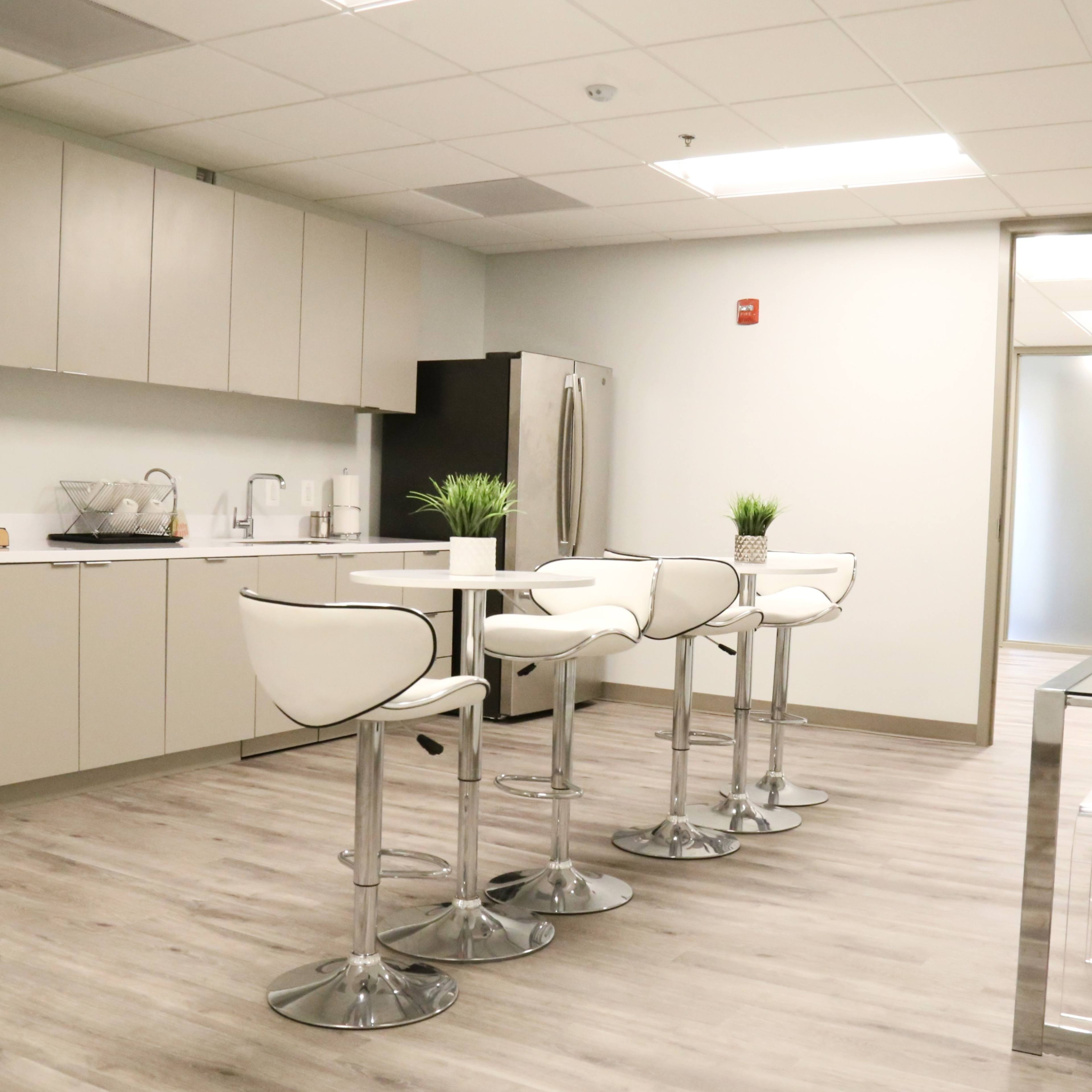 A modern kitchen area featuring sleek cabinets, a table with four high chairs, and stainless steel appliances.