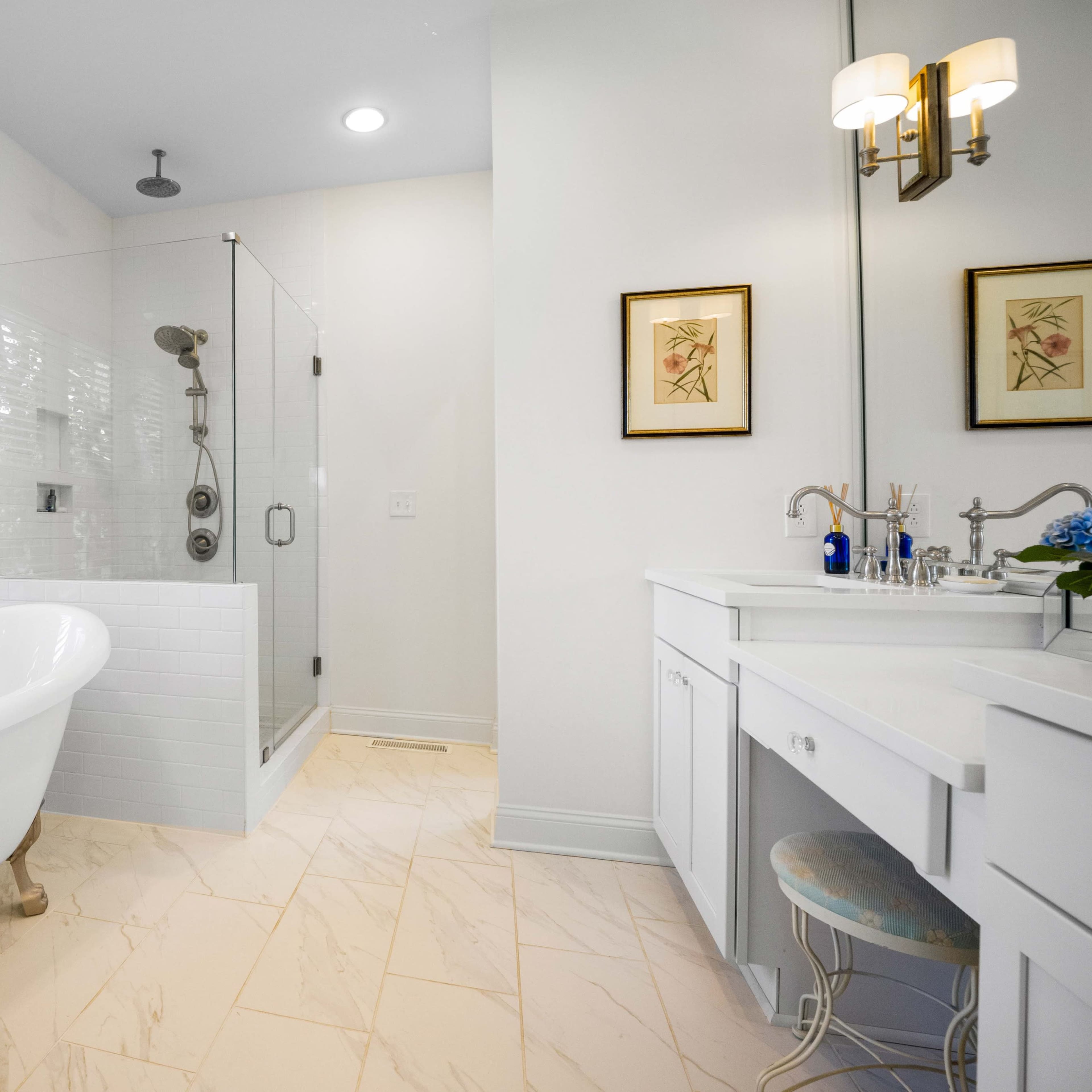 A modern bathroom featuring a freestanding bathtub, a glass shower enclosure, and a double vanity with framed artwork on the walls.