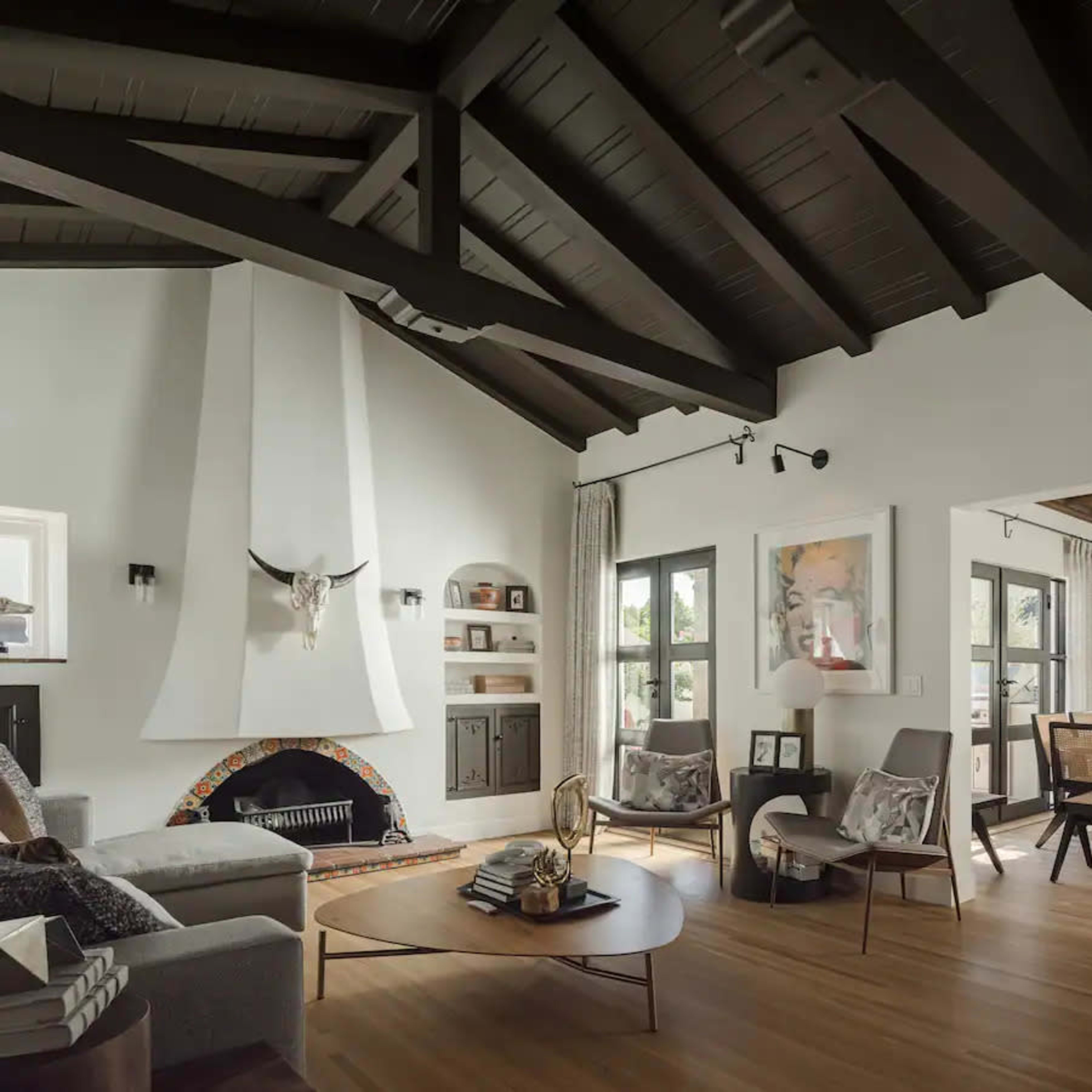 A spacious living room features high wooden ceilings, a modern fireplace with a decorative element, and a connected dining area with a large table.