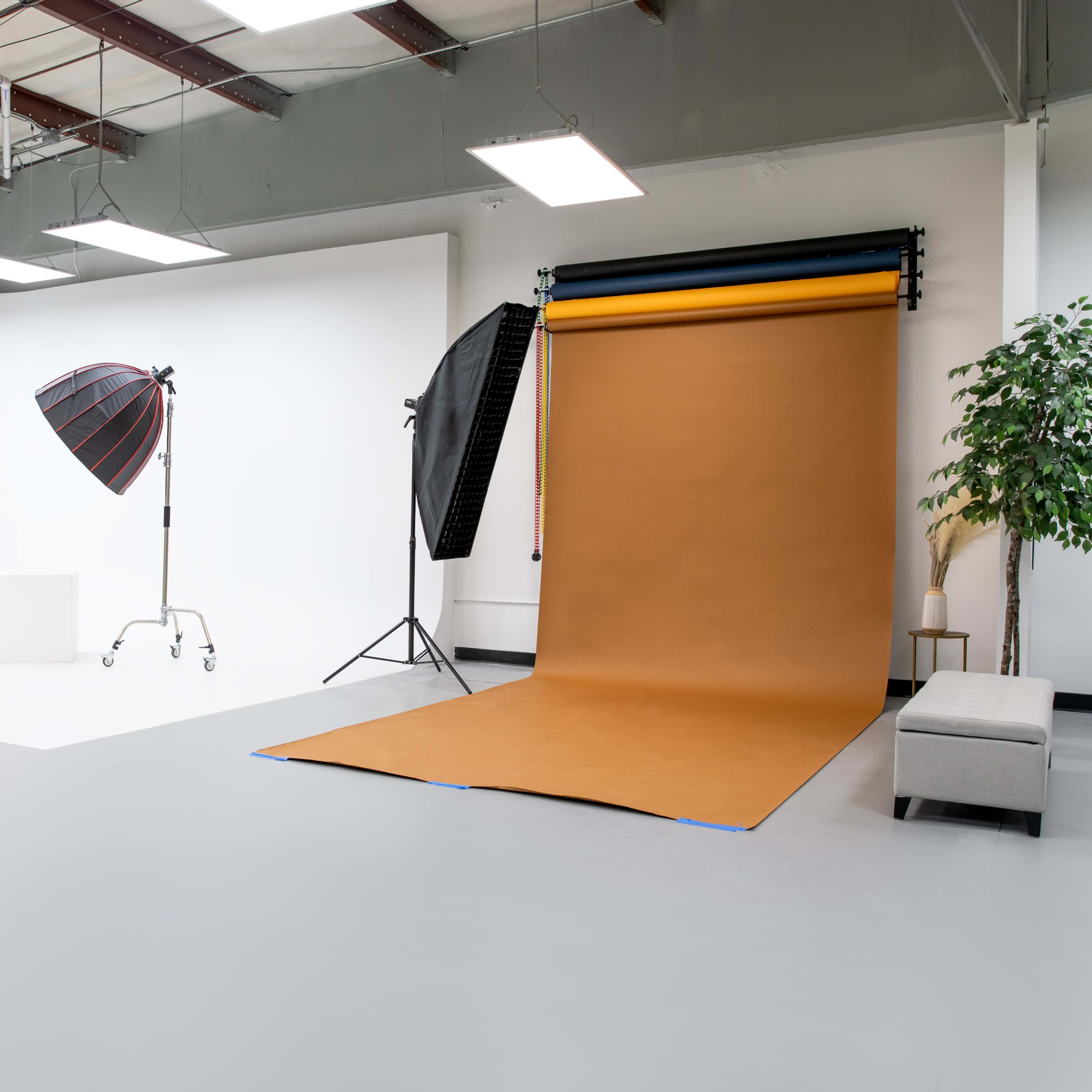A photography studio featuring a brown backdrop, lighting equipment, and a gray bench against a white wall.