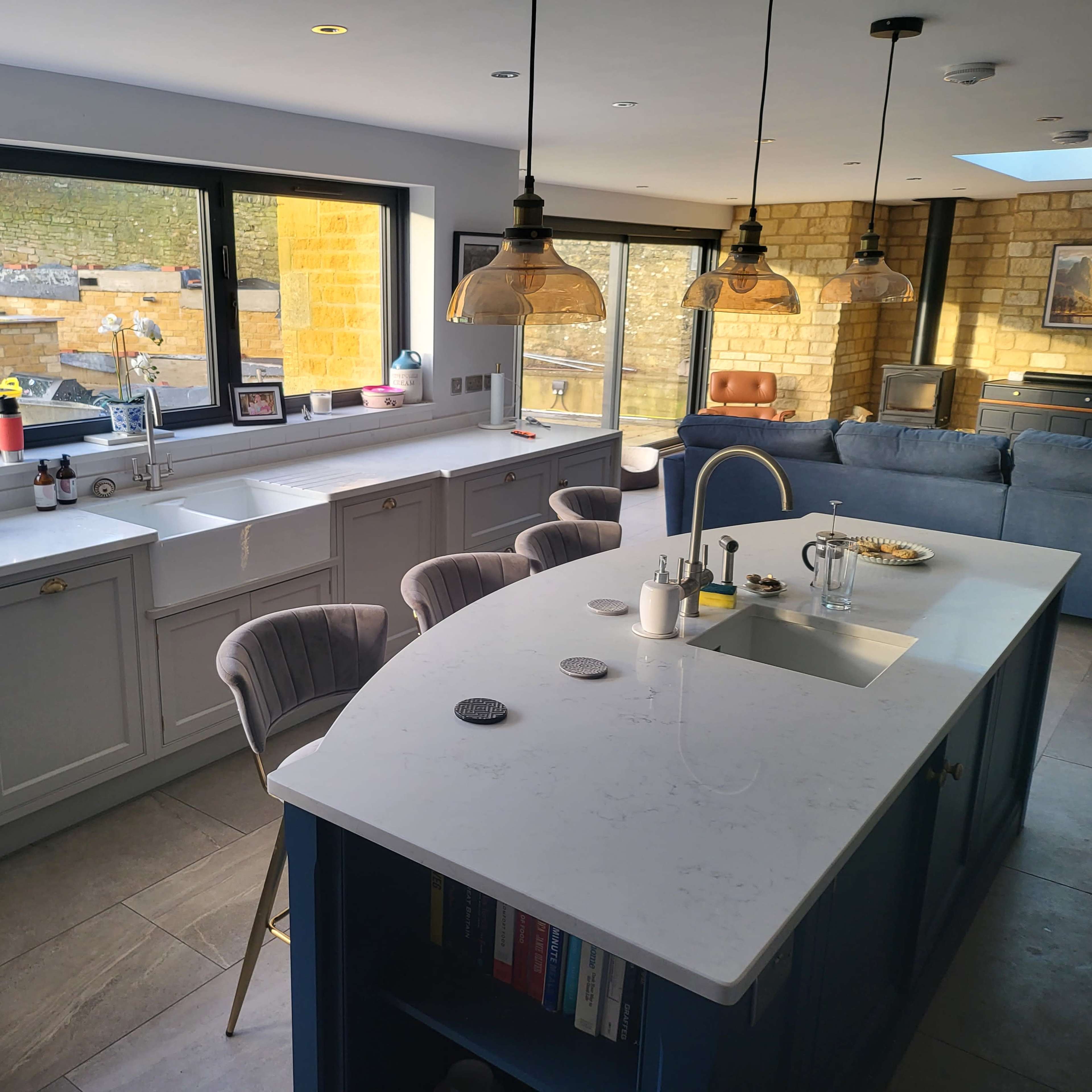 A modern kitchen with a central island, large windows providing natural light, and a living area visible in the background.