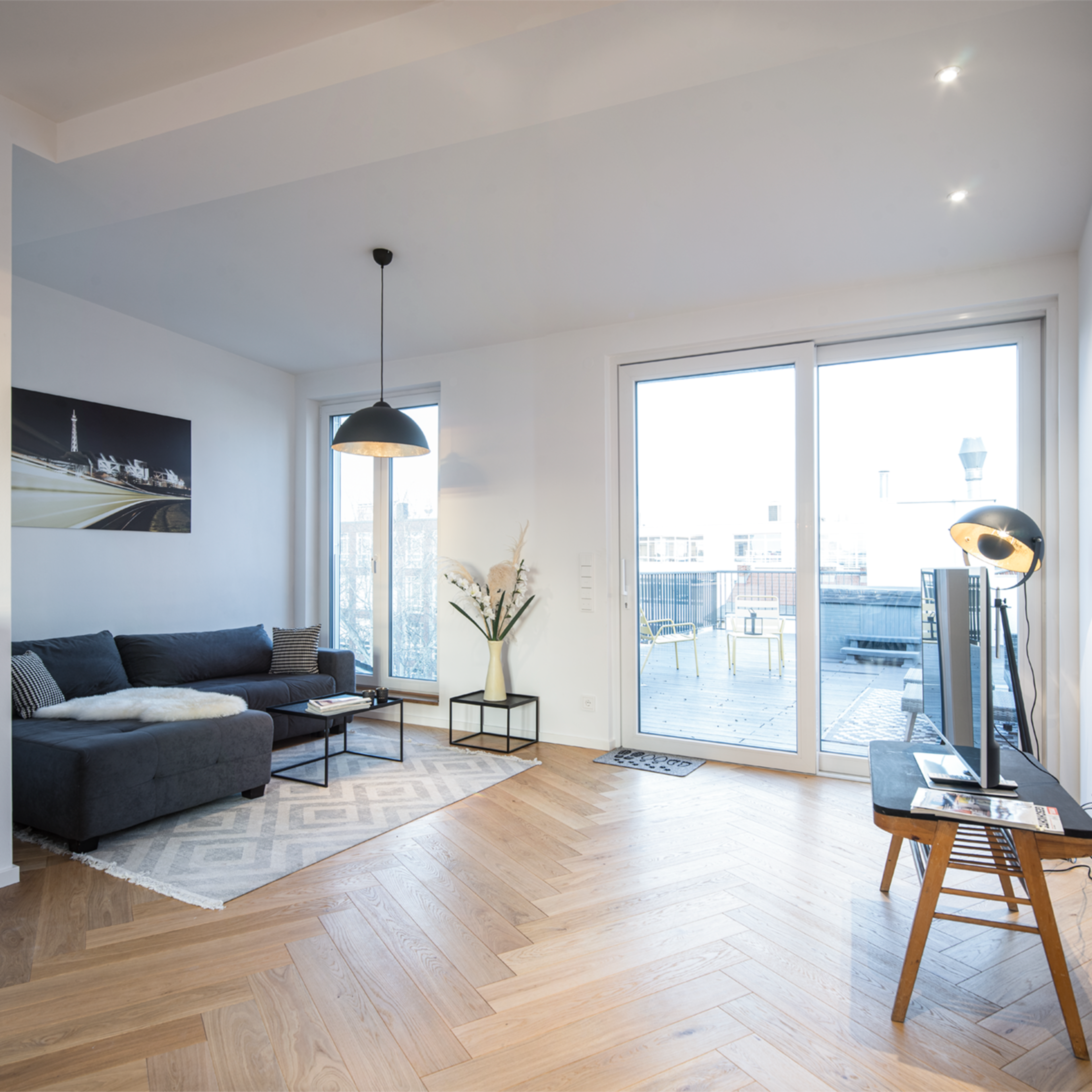 A modern living room with a gray sofa, a coffee table, large windows revealing an outdoor area, and minimalist decor.