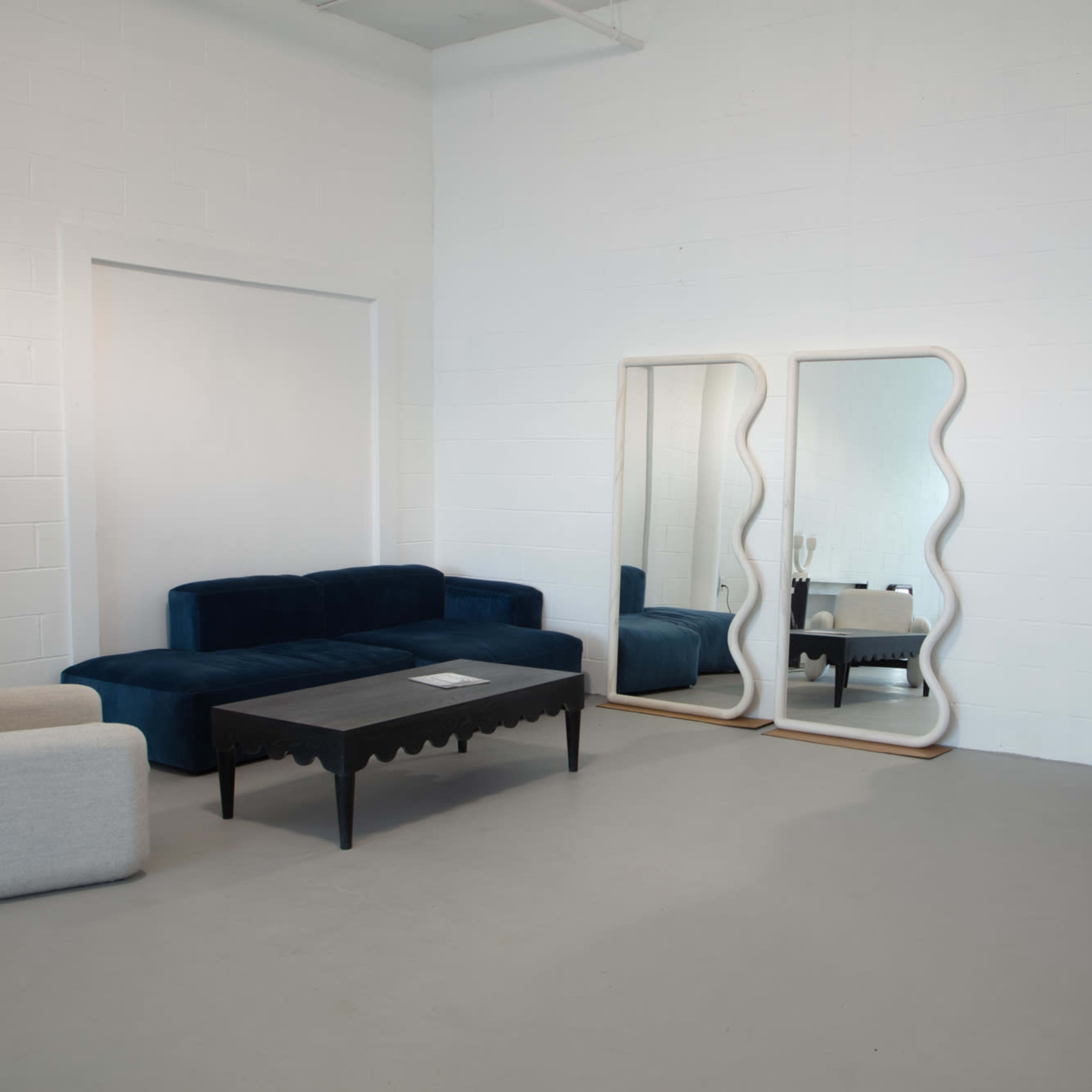A minimalist room features a blue sofa, a black table, and two large mirrors against a white wall.