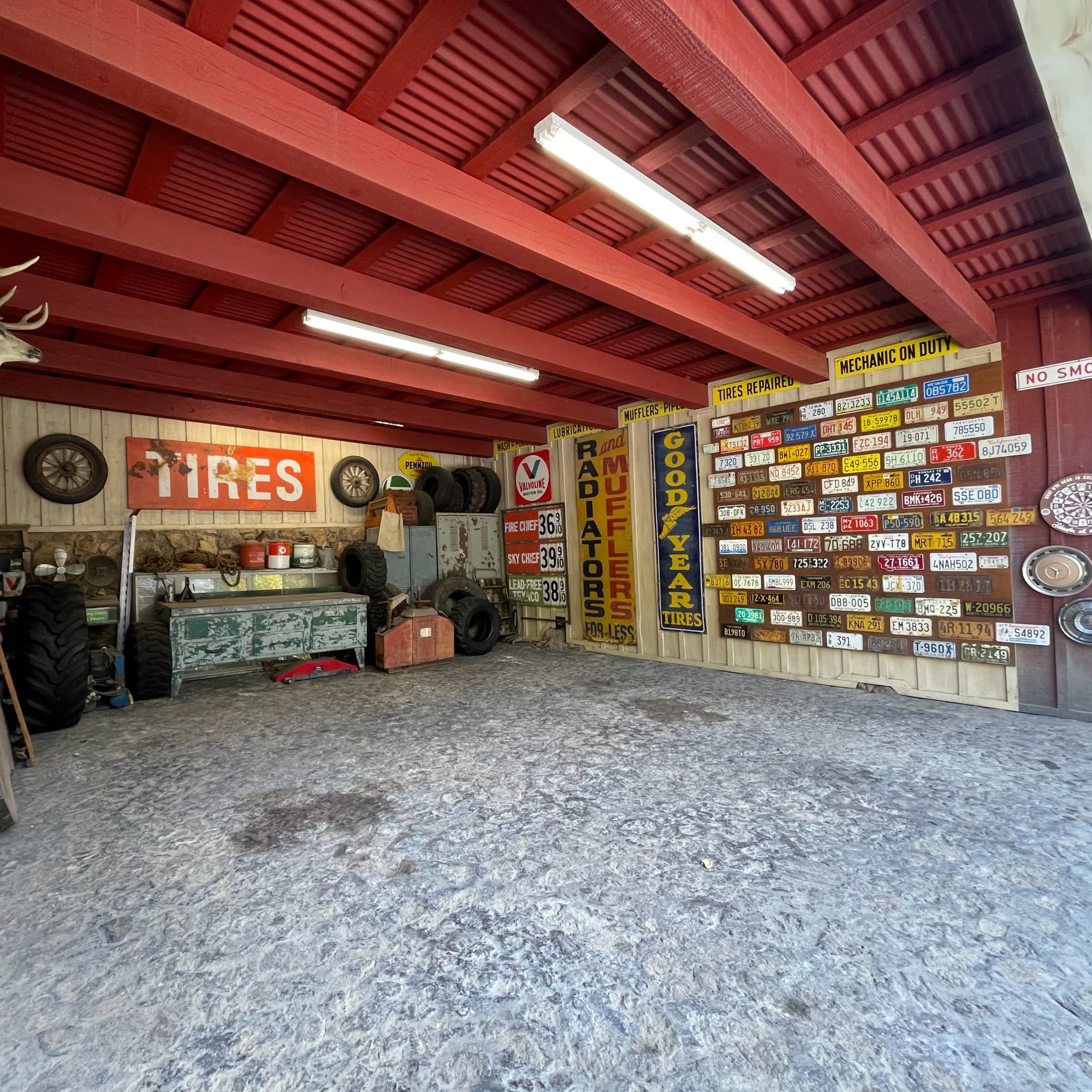 A vintage garage interior with wooden red beams, various tire advertisements, and old tools on display.