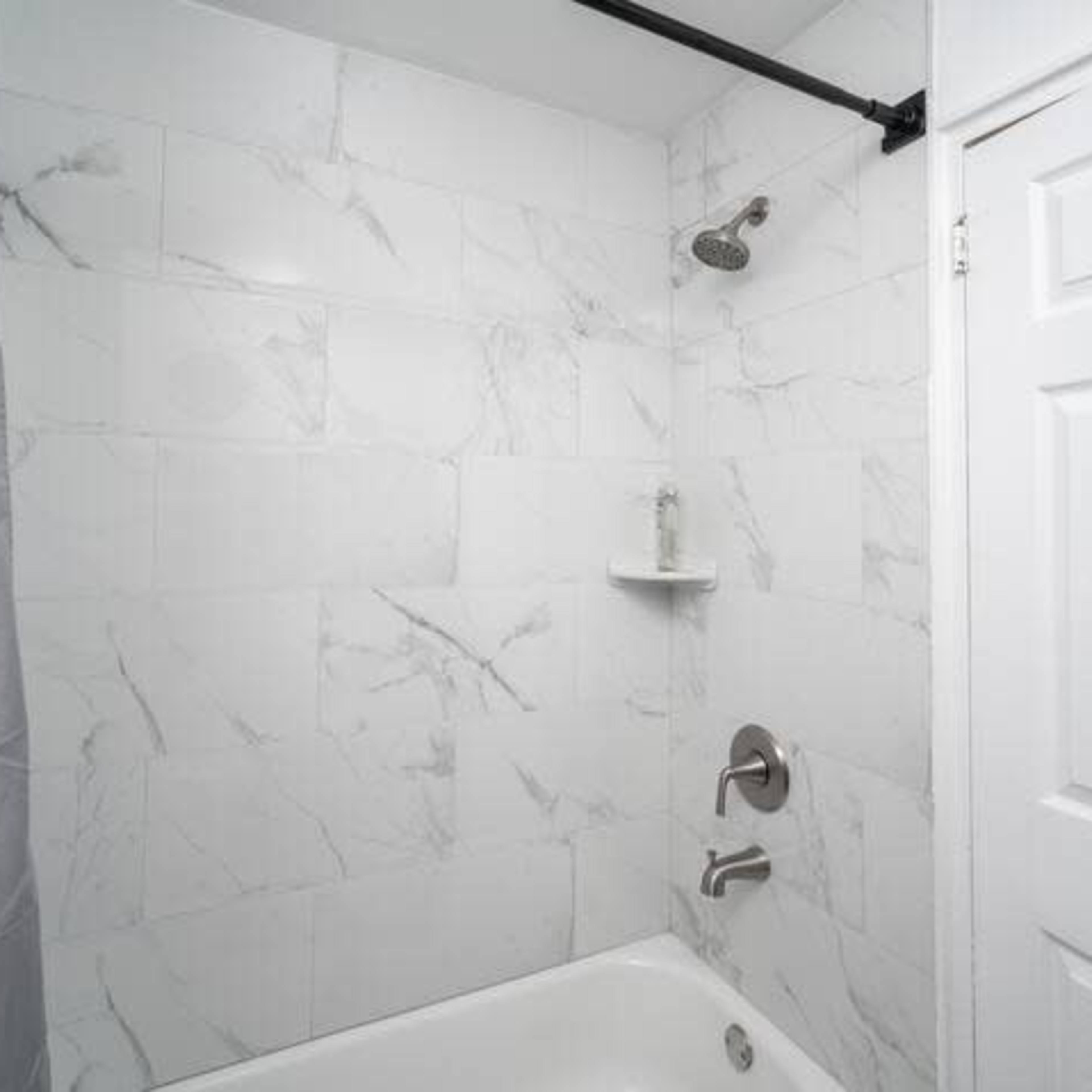 A shower area with marble-patterned tiles, a showerhead, and a white tub, alongside a closed door.