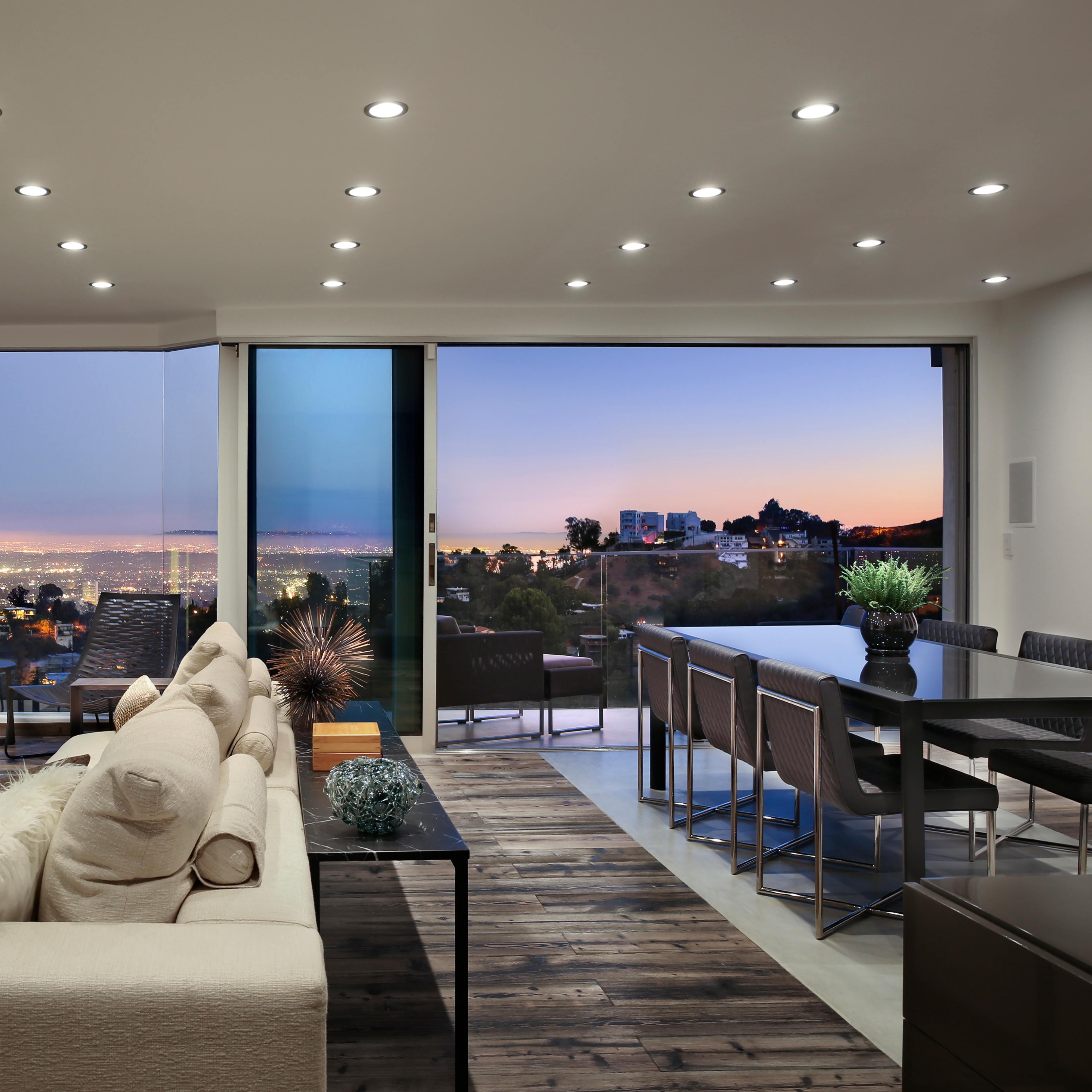 A modern living space with large windows offering a panoramic view of a city skyline at sunset.