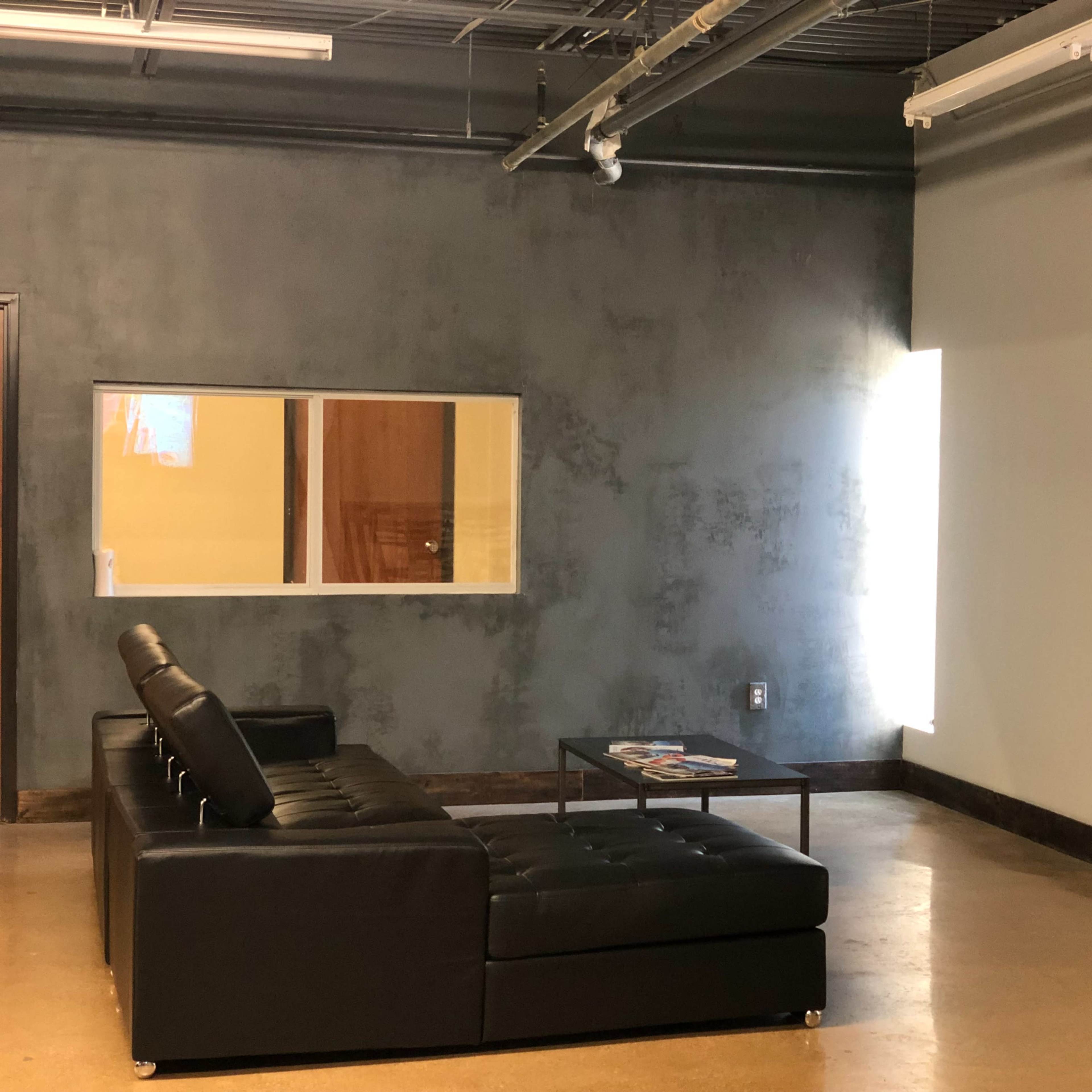 A modern lounge area featuring a black sectional couch, a coffee table with magazines, and a wall-mounted television.