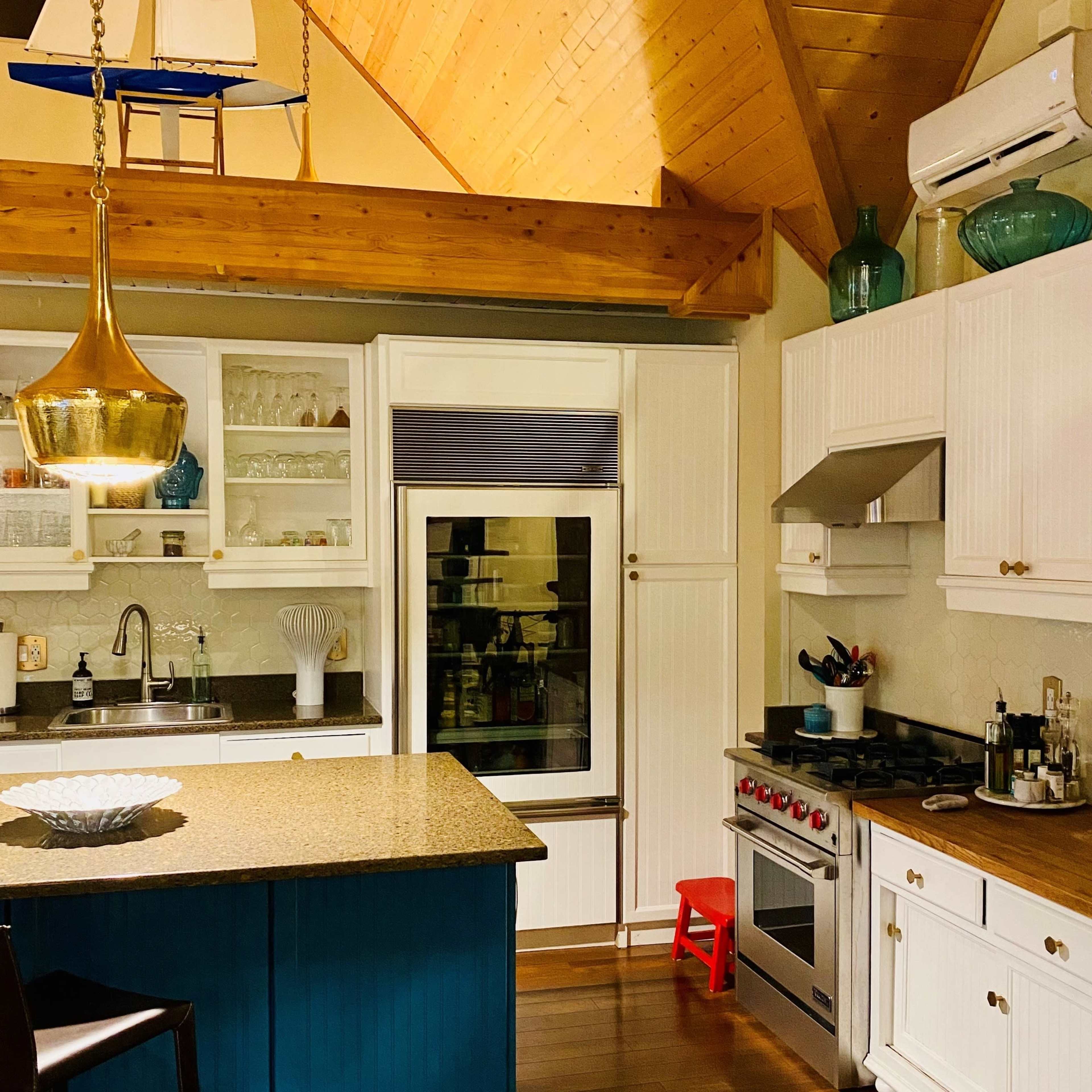 A modern kitchen with white cabinetry, a central blue island, and wooden accents, featuring a stove and a glass refrigerator.