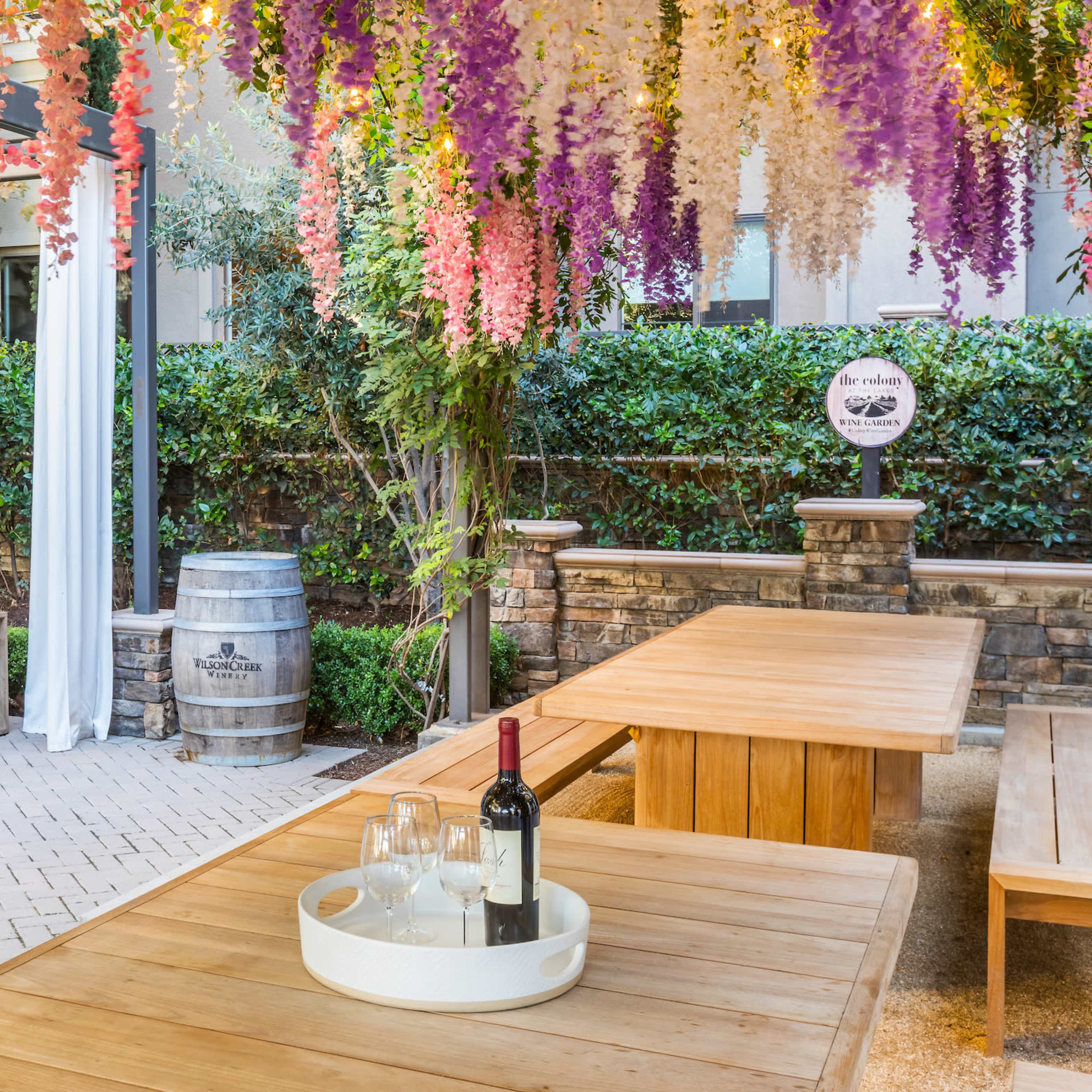 A patio area features wooden tables and seating, decorated with hanging floral arrangements and a wine bottle with glasses on a tray.