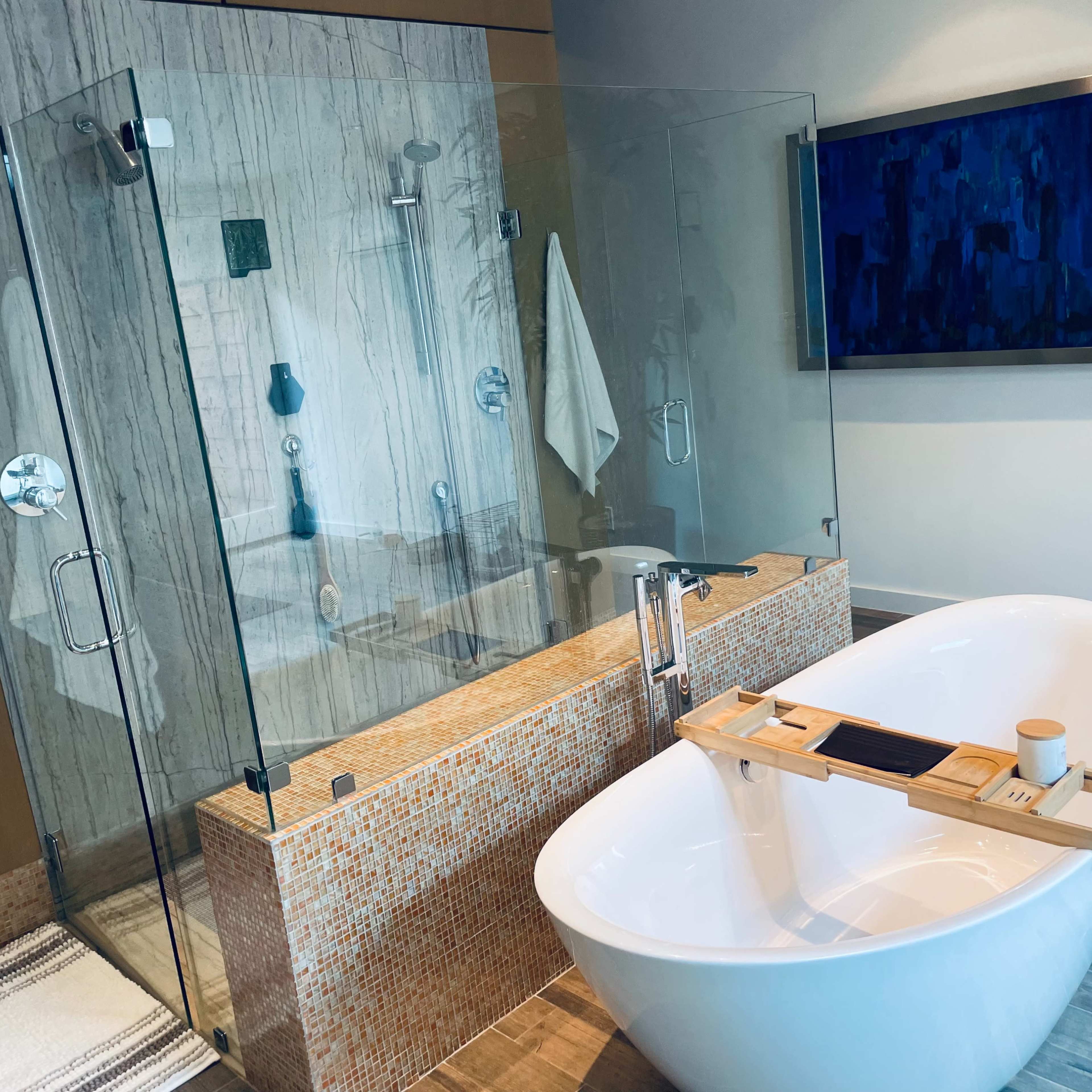 A modern bathroom features a glass-enclosed shower next to a freestanding bathtub, with a wooden bath tray placed across the tub.