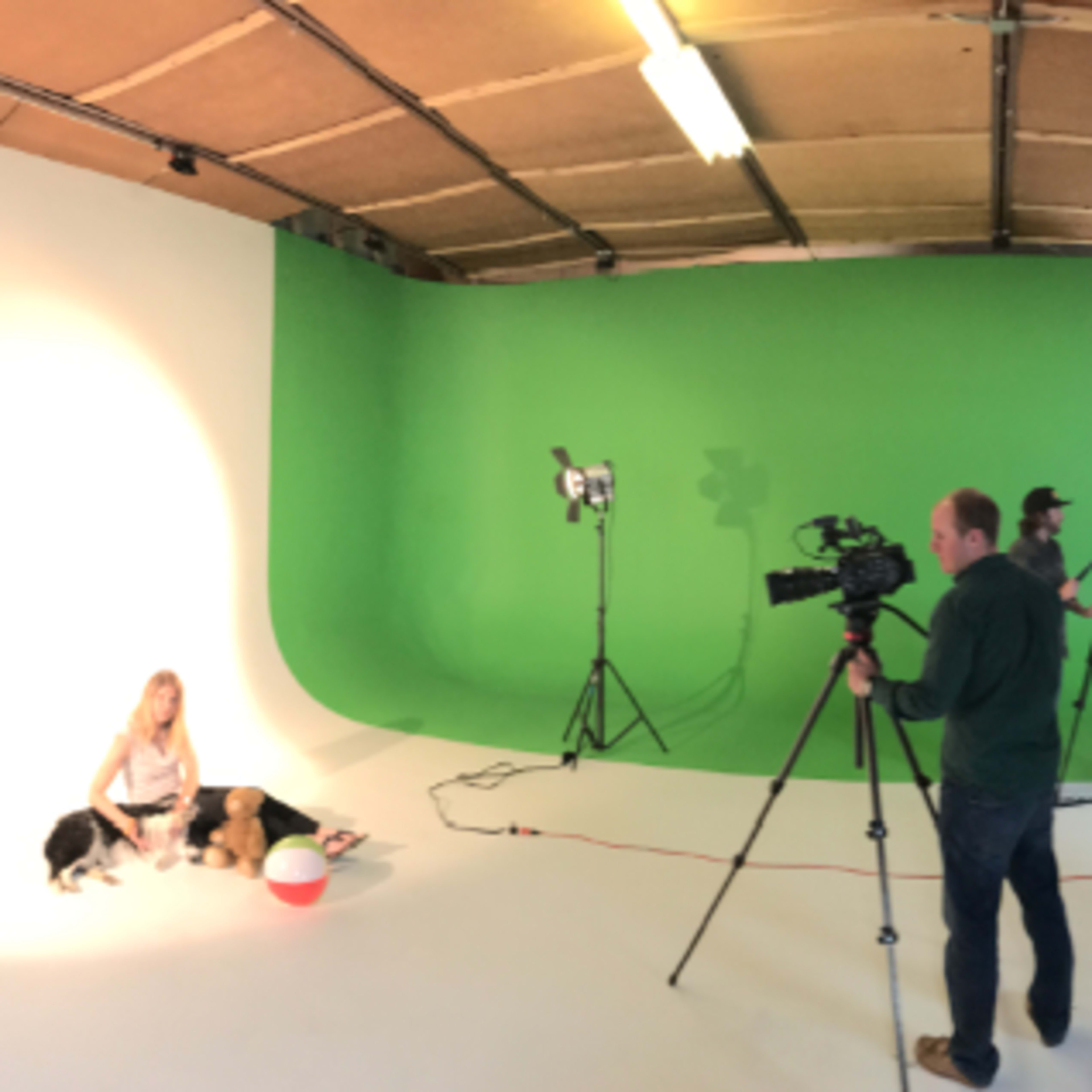 A panoramic view of a studio showing different shooting areas, including a kitchen setup, a green screen, and various crew members preparing for a shoot.