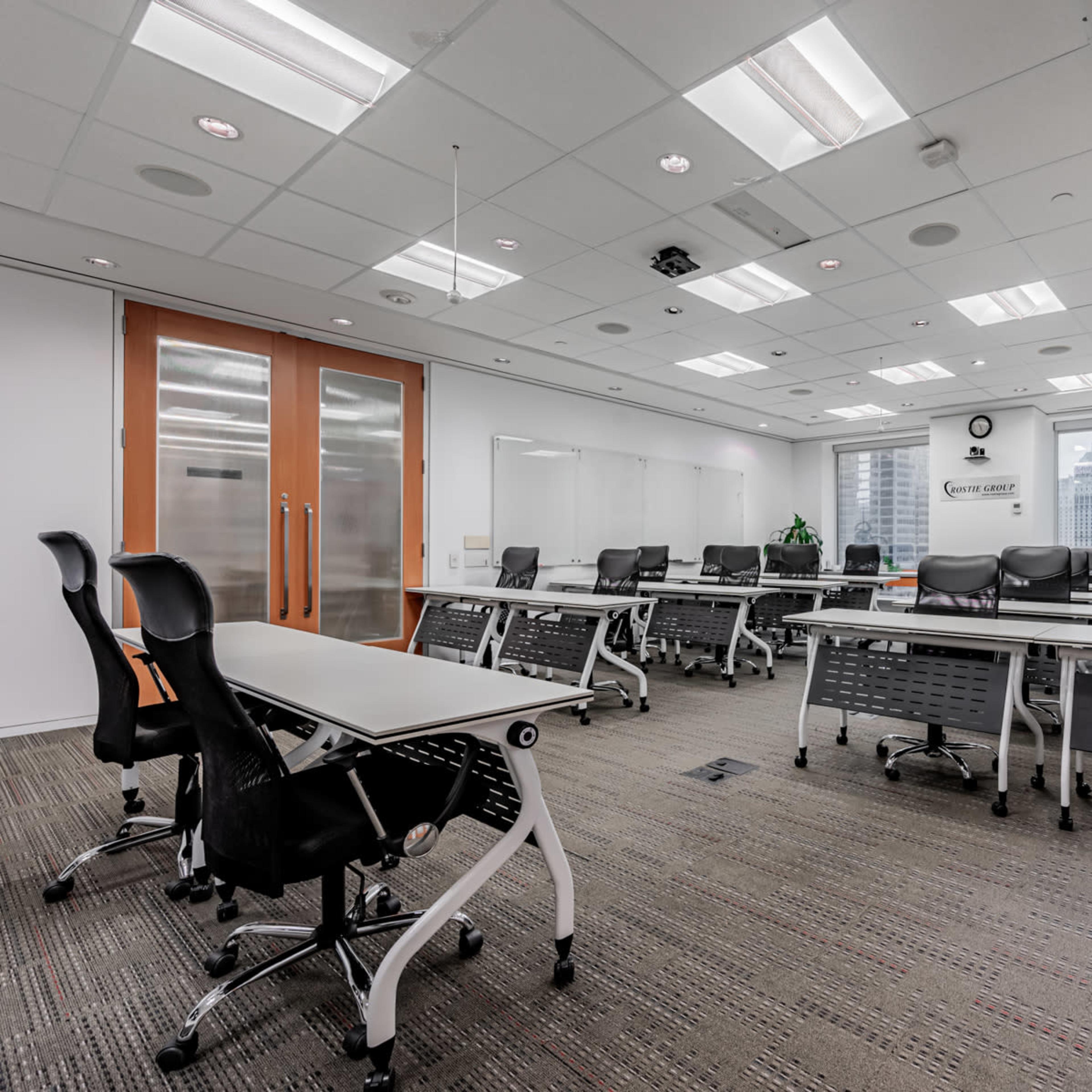 A bright, modern office conference room features several tables and chairs arranged for a meeting, with large windows overlooking a cityscape.