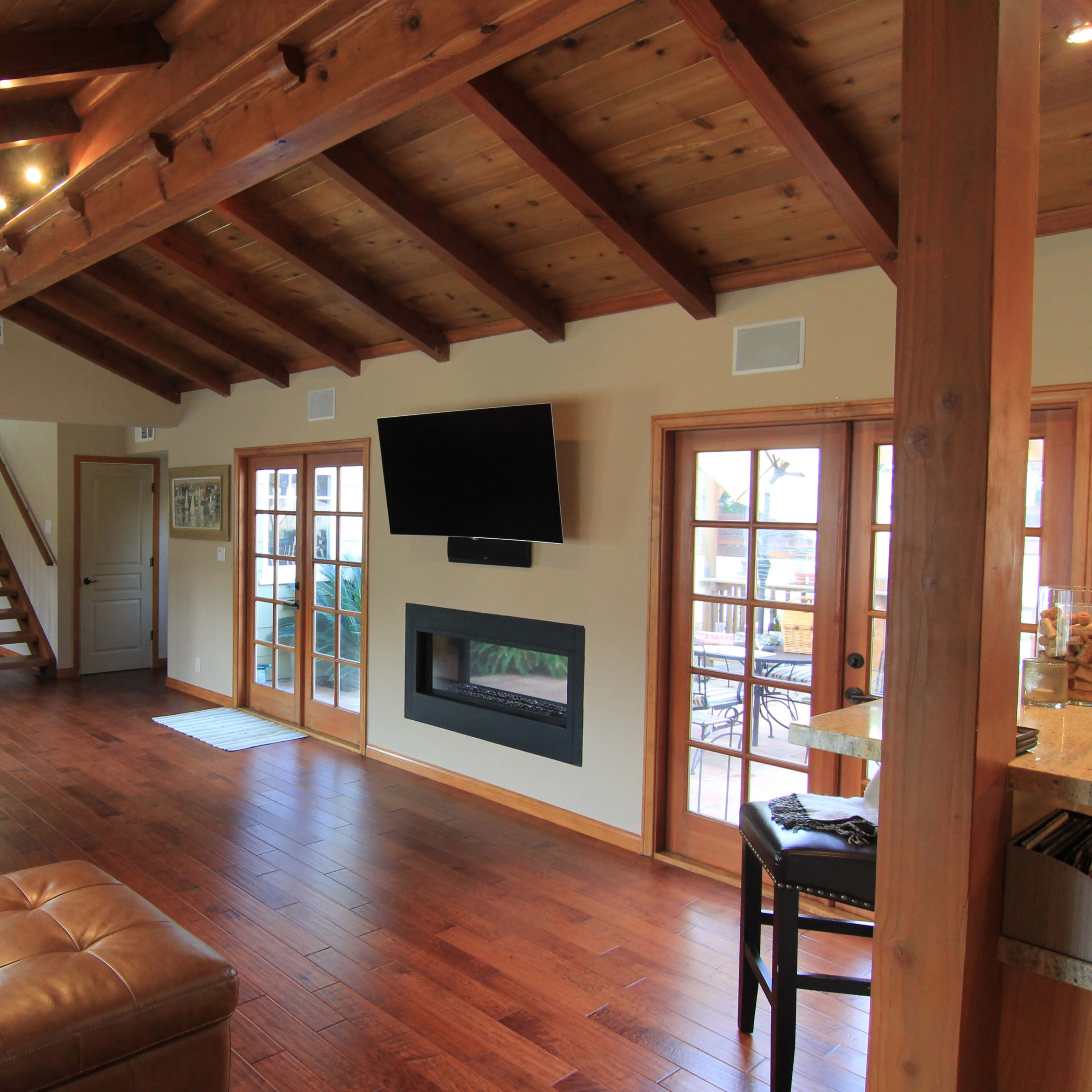 A spacious living room with wooden beams, a grand piano, a leather sofa, and a modern fireplace.