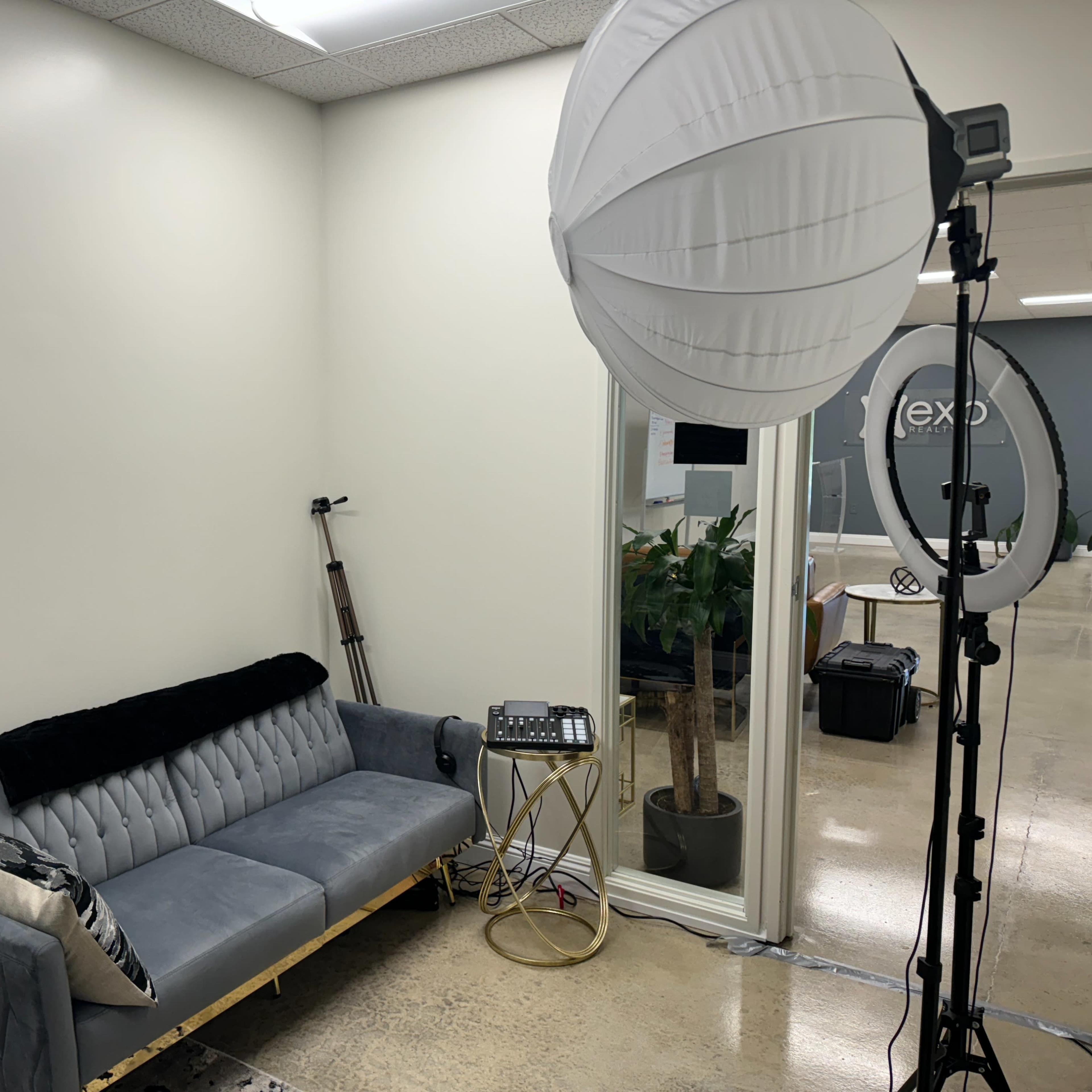 A modern office space with a gray sofa, a round light diffuser, and a small table, featuring a plant visible through a glass partition.