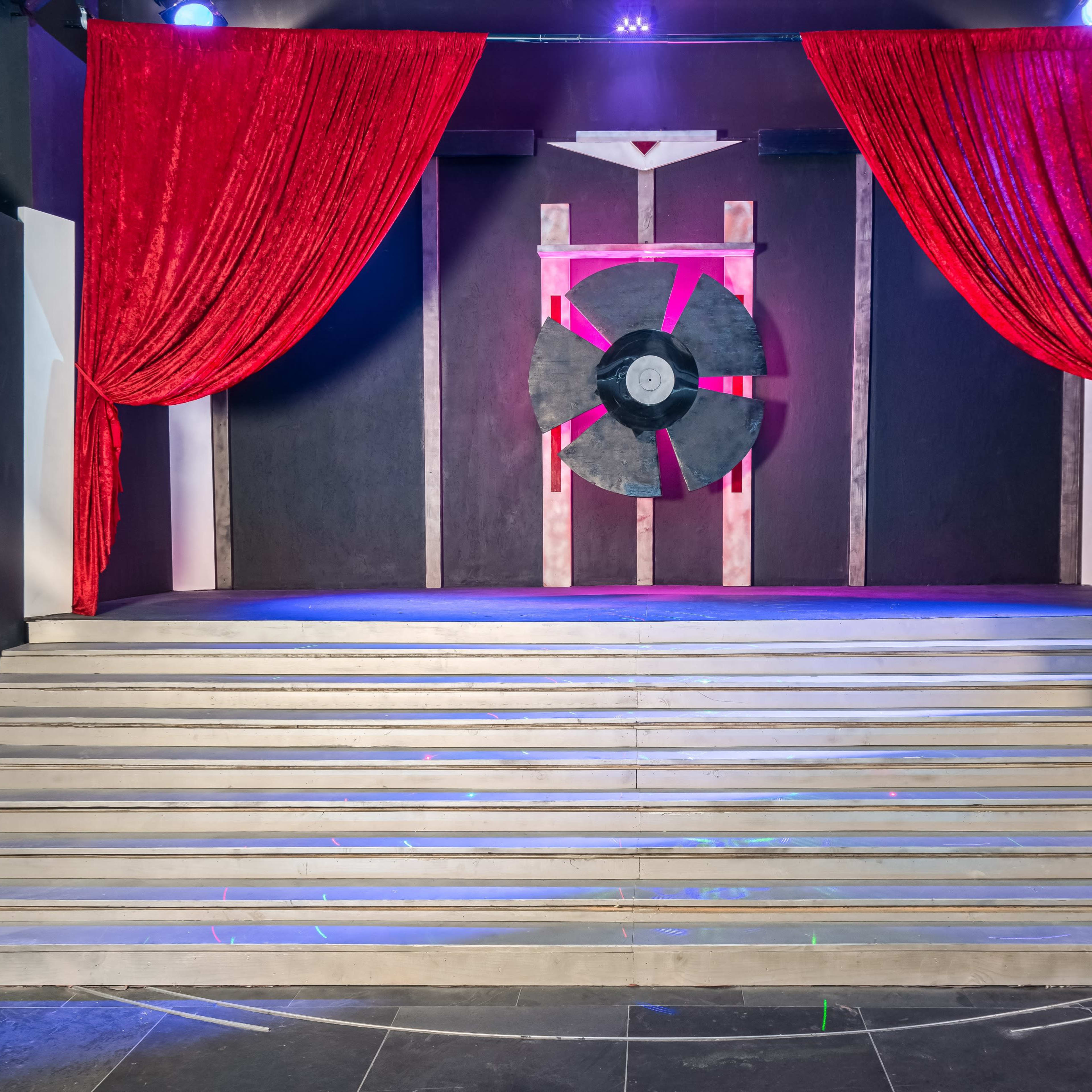 A stage with a set of stairs leading up to a backdrop featuring a large black fan and red curtains draped on either side.