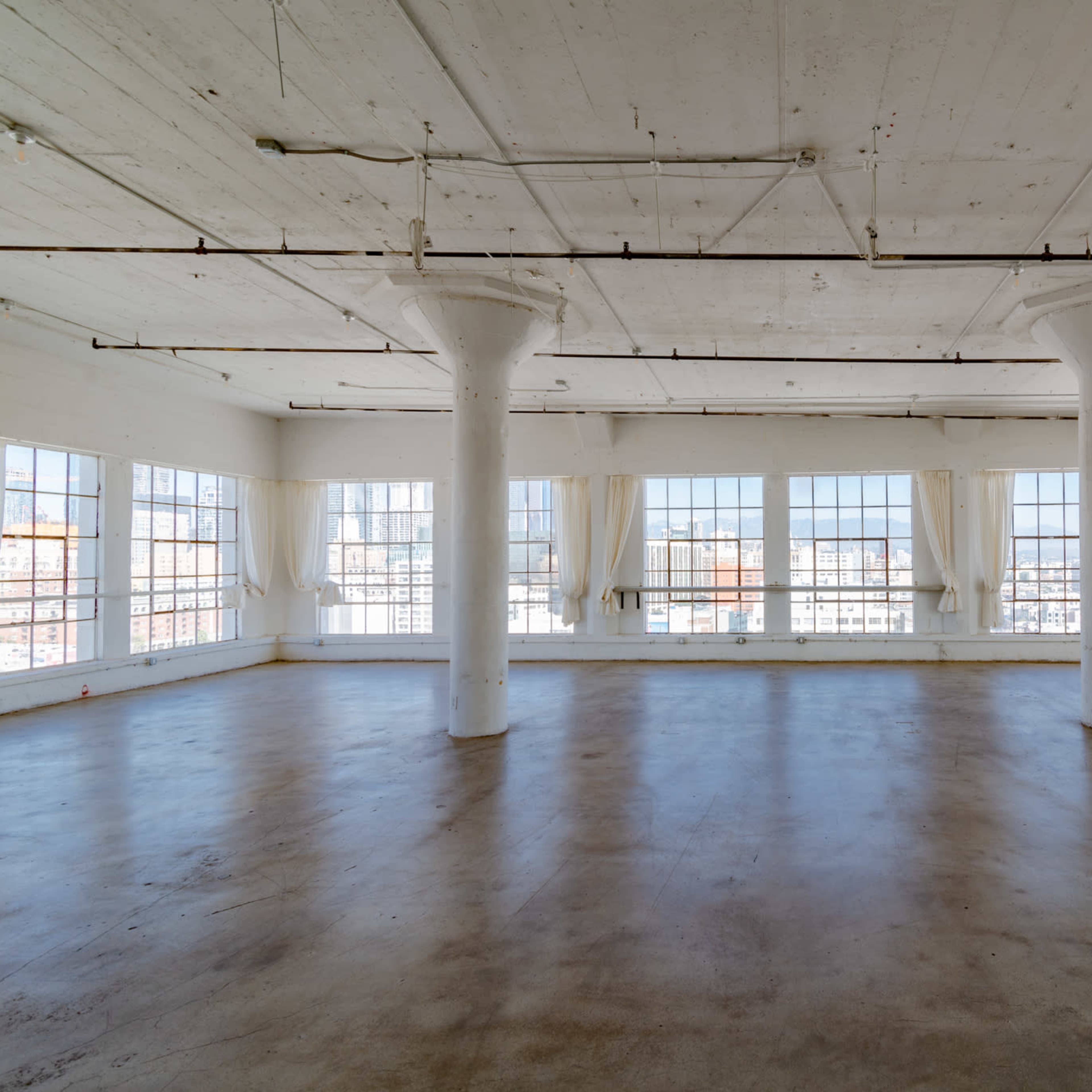 An empty, well-lit industrial space with large windows and concrete flooring.