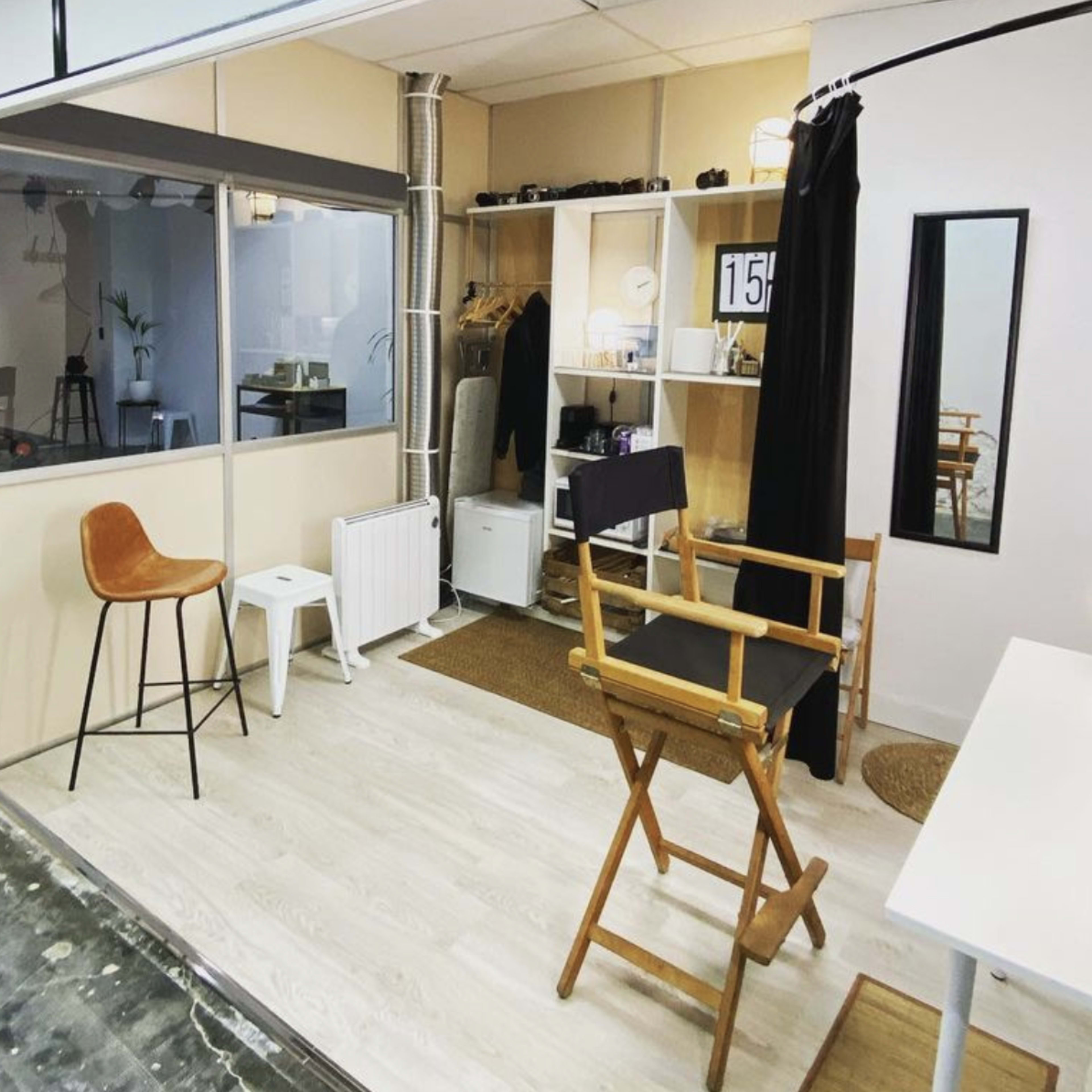 A well-lit studio space featuring a makeup station with a mirror, a director's chair, and various furniture arranged neatly on a wooden floor.