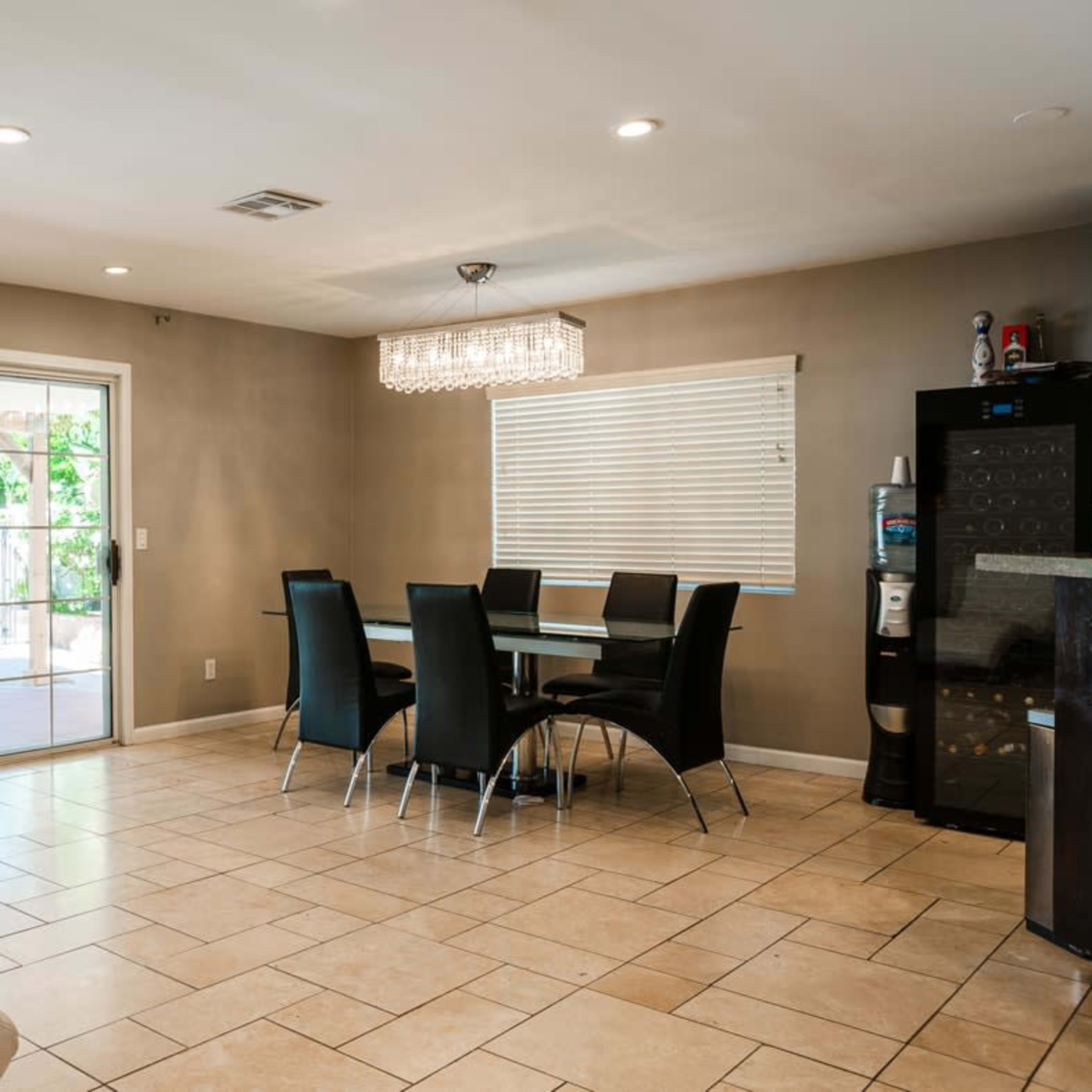 A dining area features a glass table surrounded by black chairs, with a sliding glass door leading to an outdoor space.