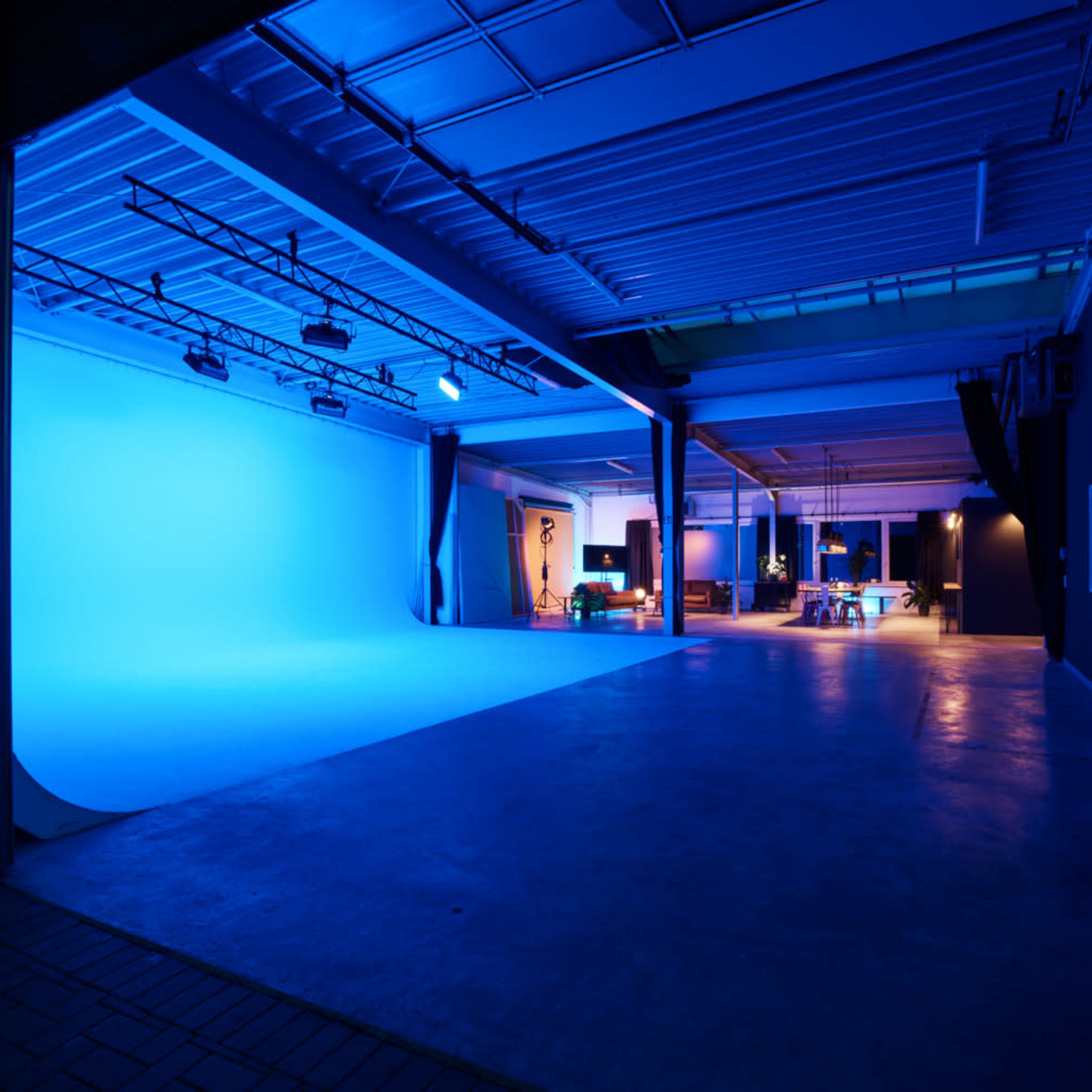 A spacious studio with a blue backdrop, bright lights, and a modern setting featuring a work area and seating.