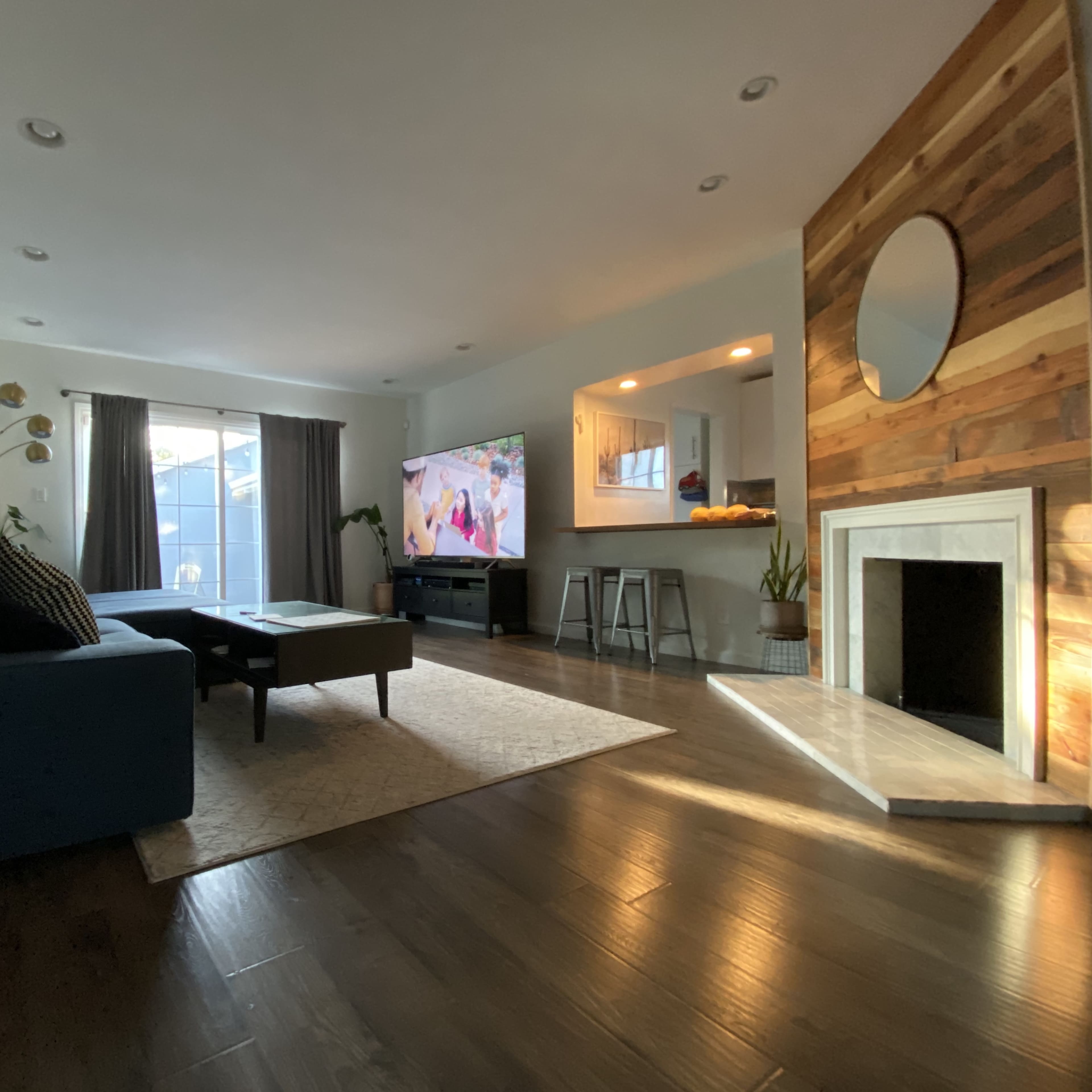 A living room with a blue couch, a coffee table, a television against one wall, and a fireplace with a circular mirror above it.