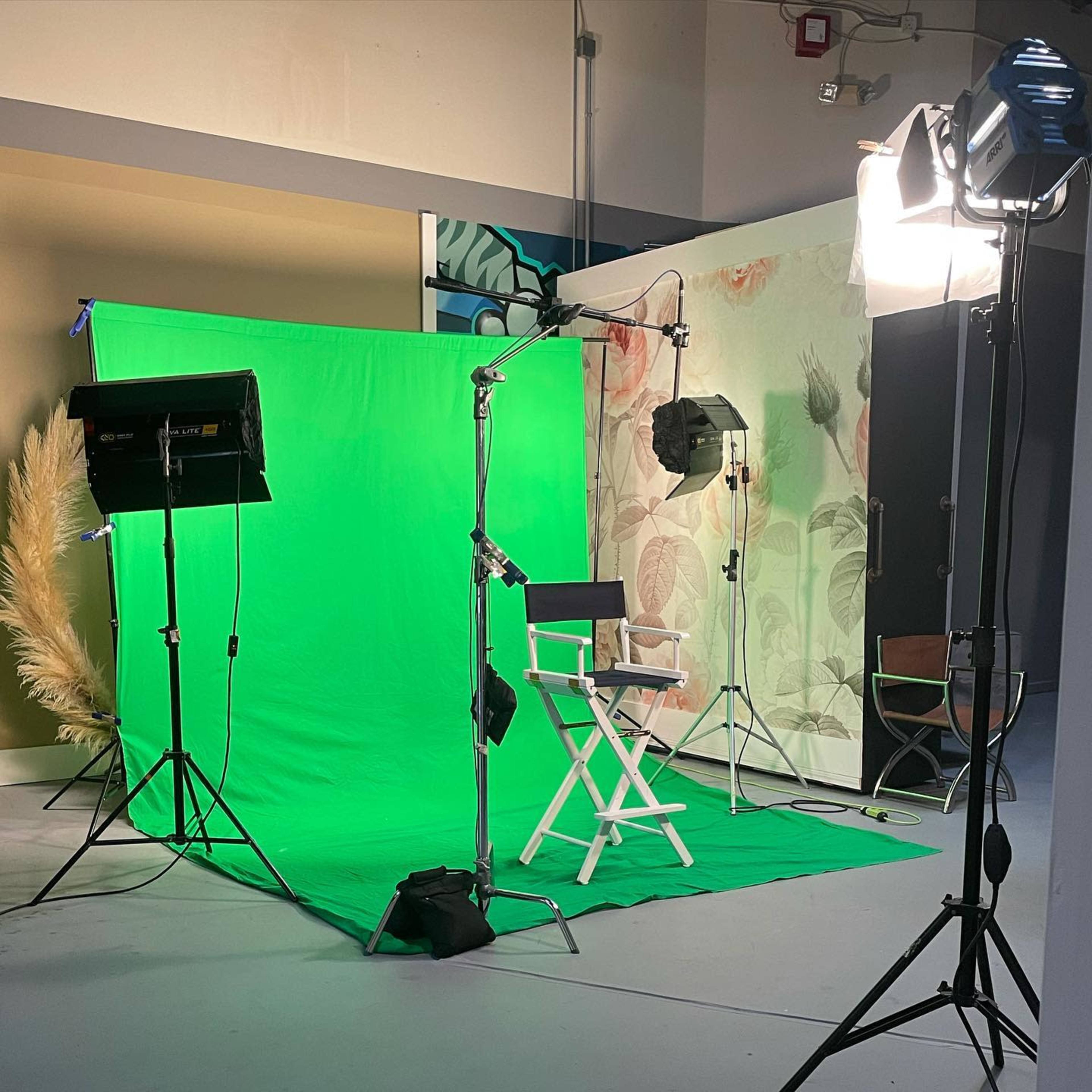 A photography or video setup with a green screen, lighting equipment, and a director's chair in a studio environment.