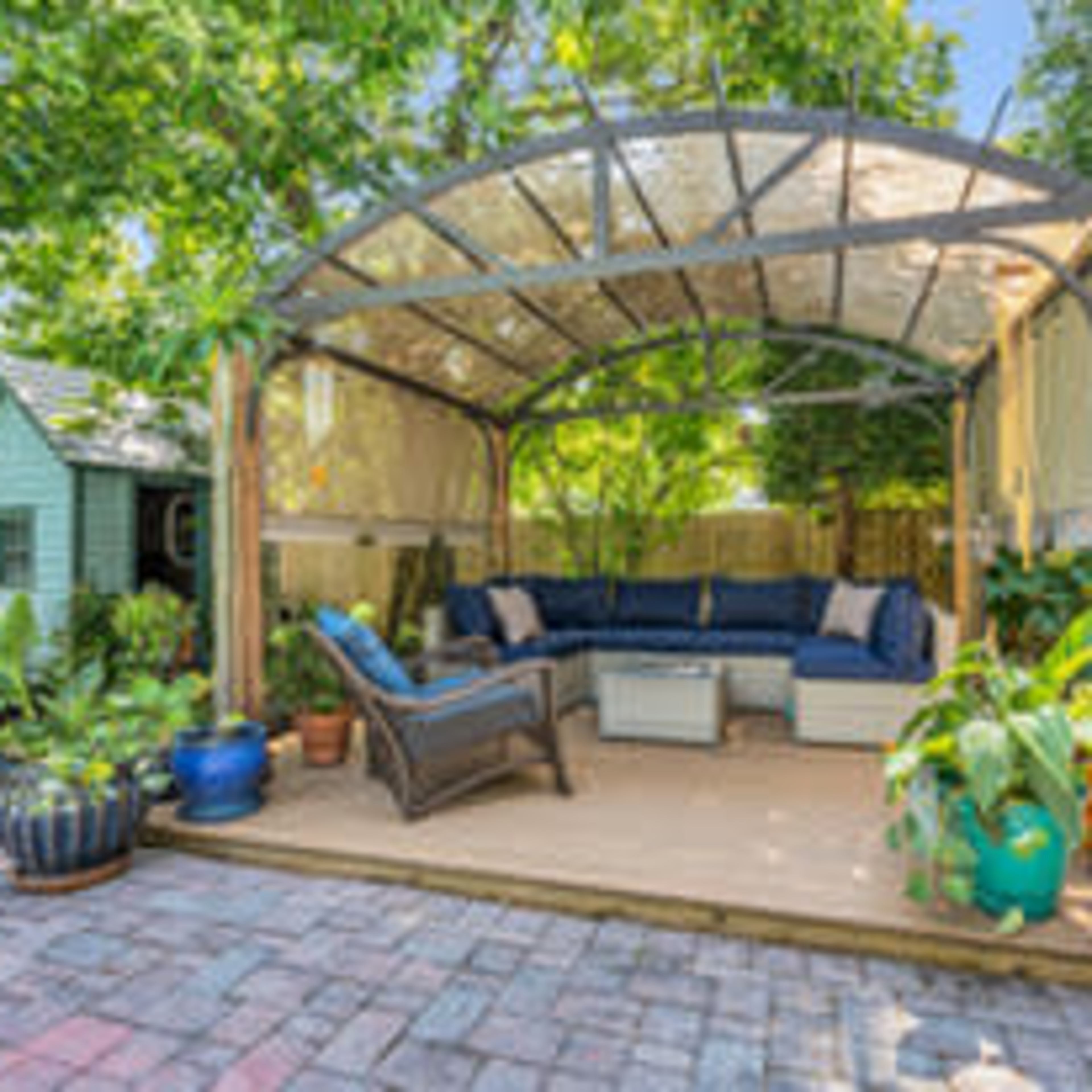 A patio with a covered seating area featuring a blue sofa, a coffee table, and various potted plants.
