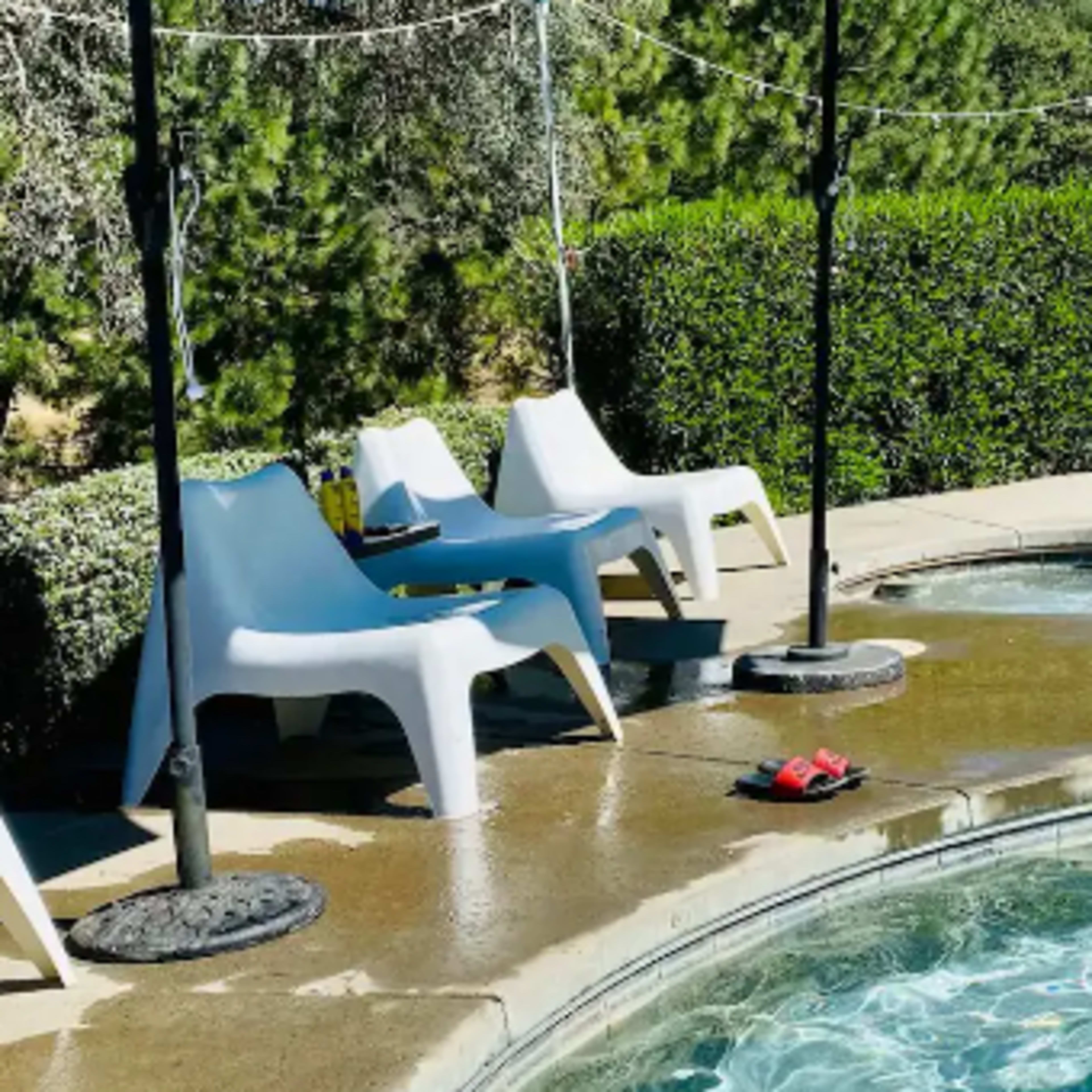 A pool area with two white lounge chairs, a small hot tub, and a patio surrounded by greenery.
