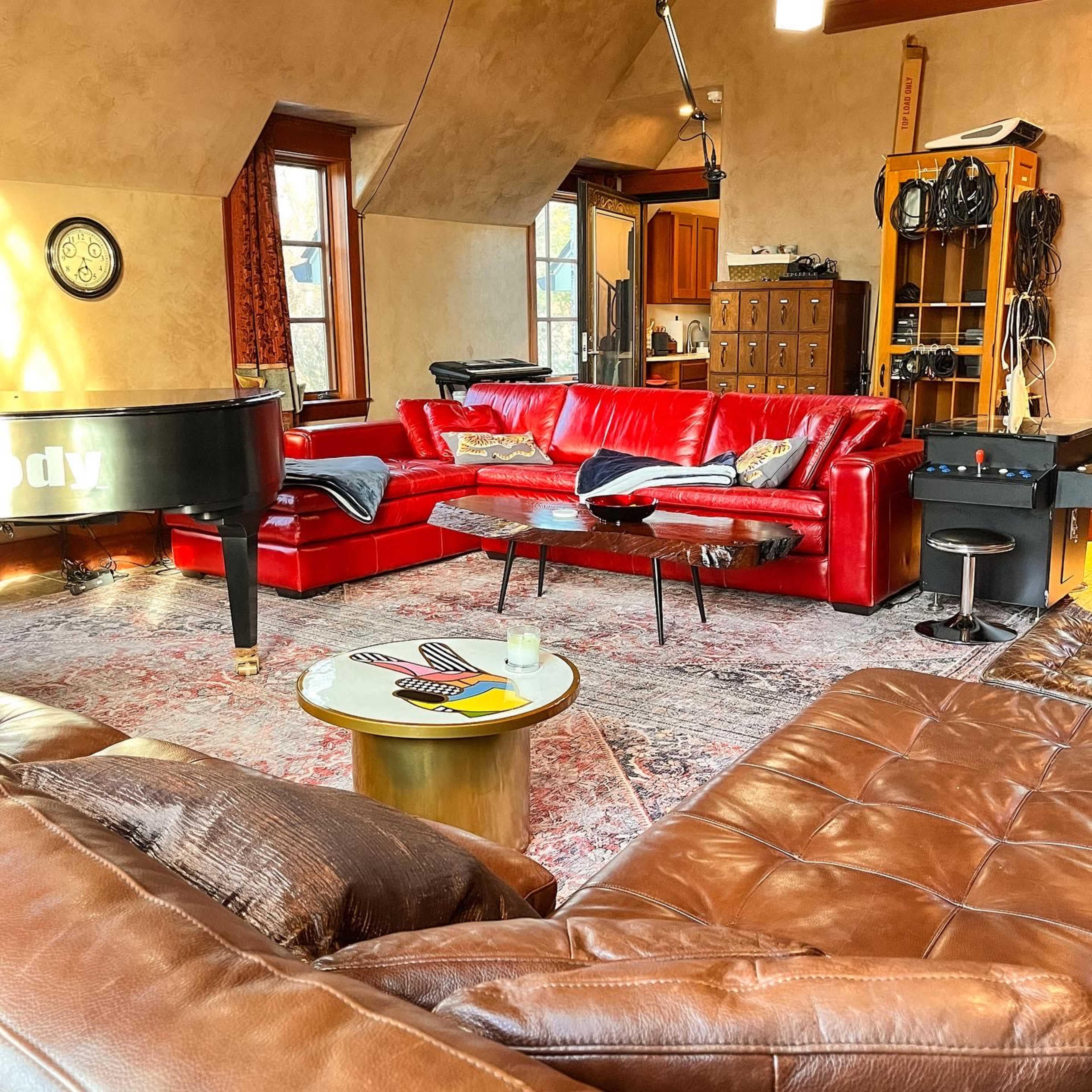 A cozy living room with red leather sofas, a grand piano, and various musical equipment.
