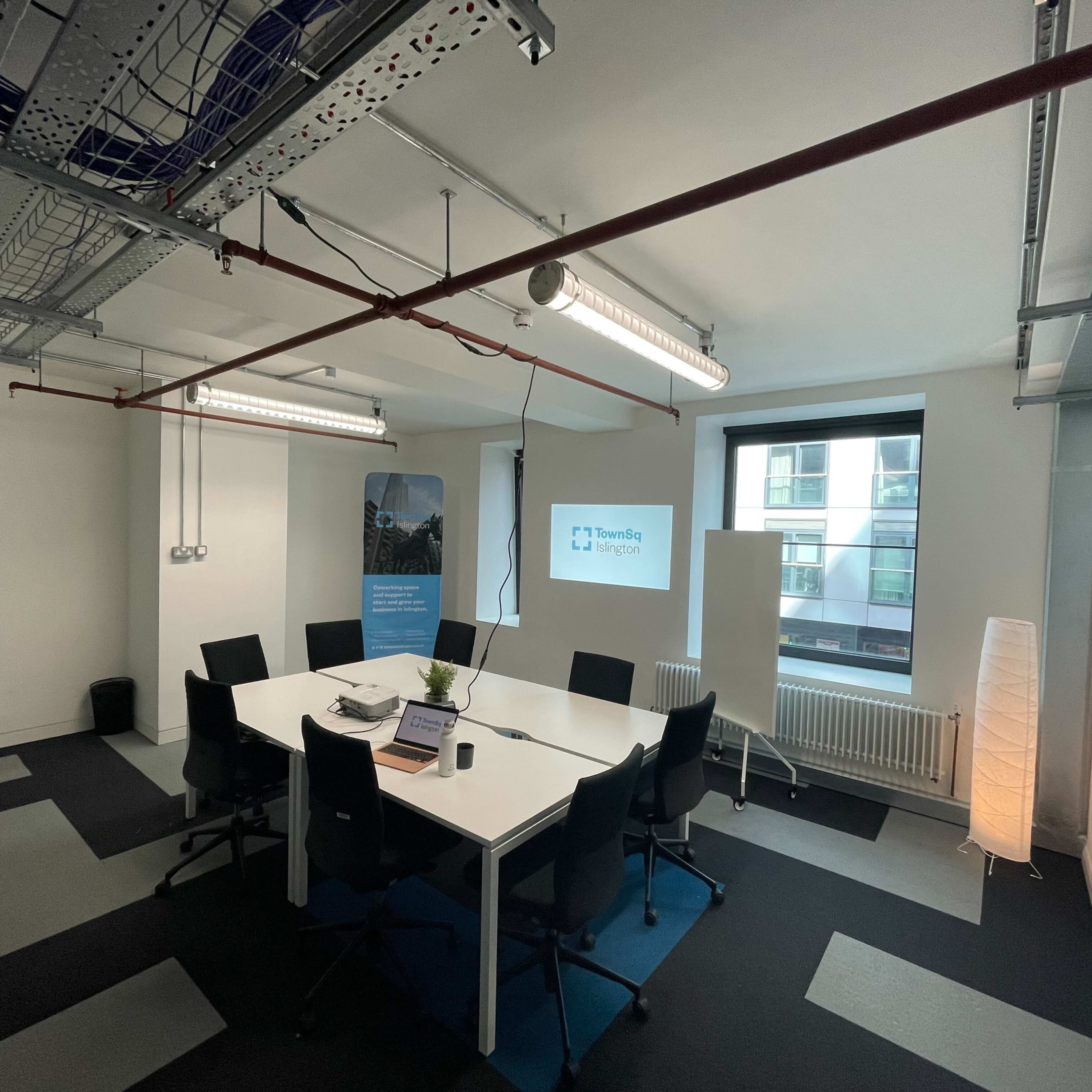 A modern office space with a white table surrounded by black chairs, a floor lamp, and a large window.