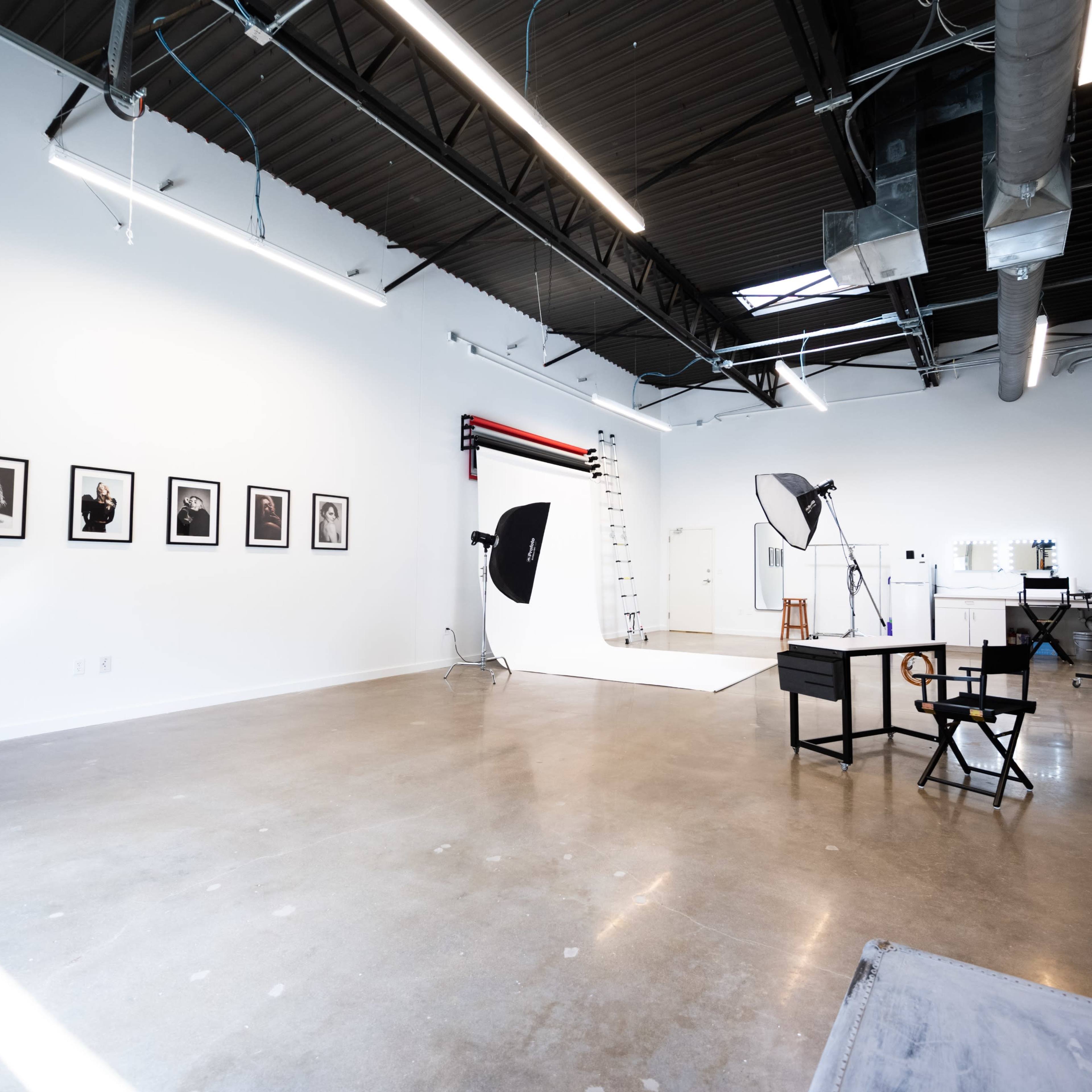 A spacious photography studio featuring a backdrop, lighting equipment, and framed photographs on the walls.