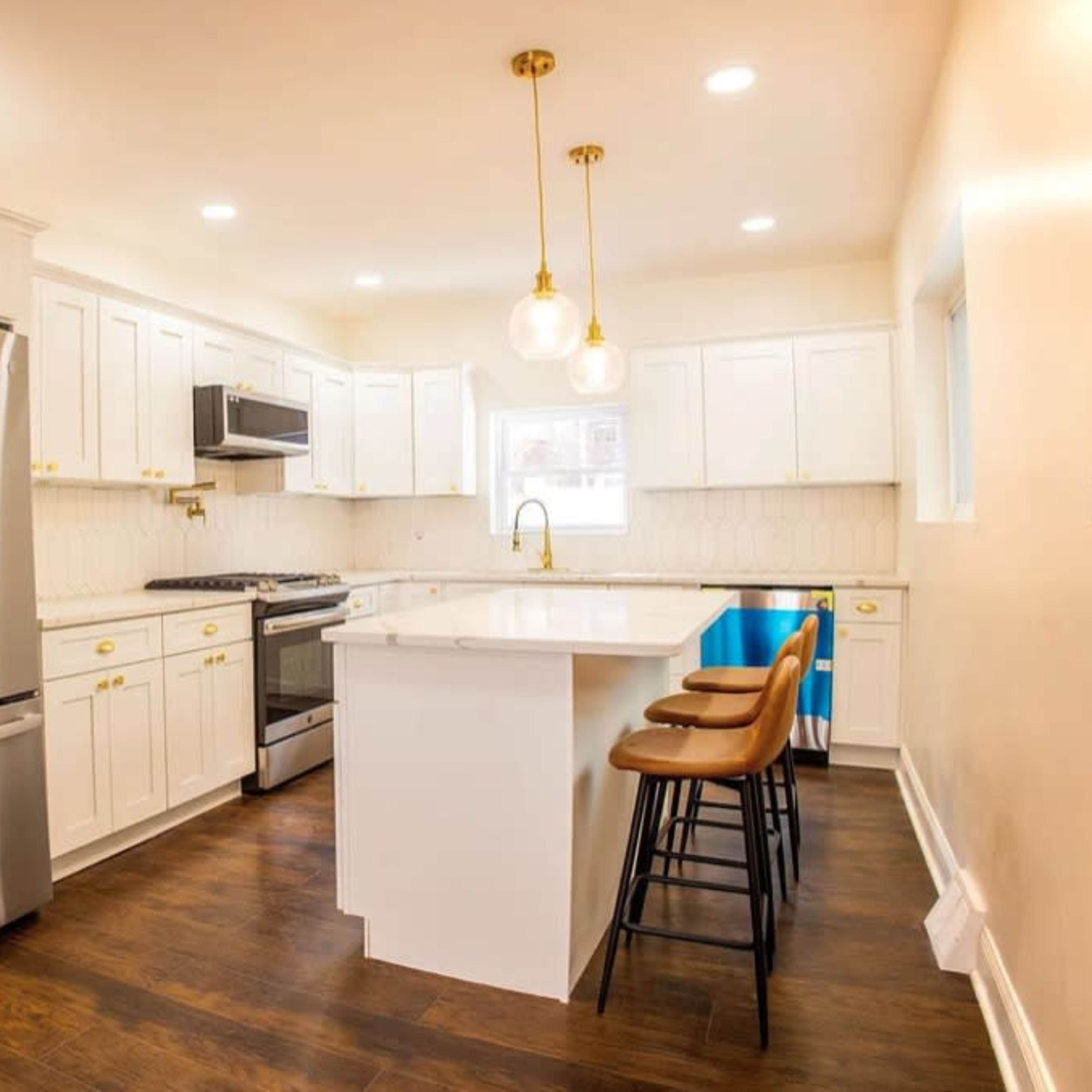 A modern kitchen featuring white cabinetry, stainless steel appliances, a center island with bar seating, and wooden floors.