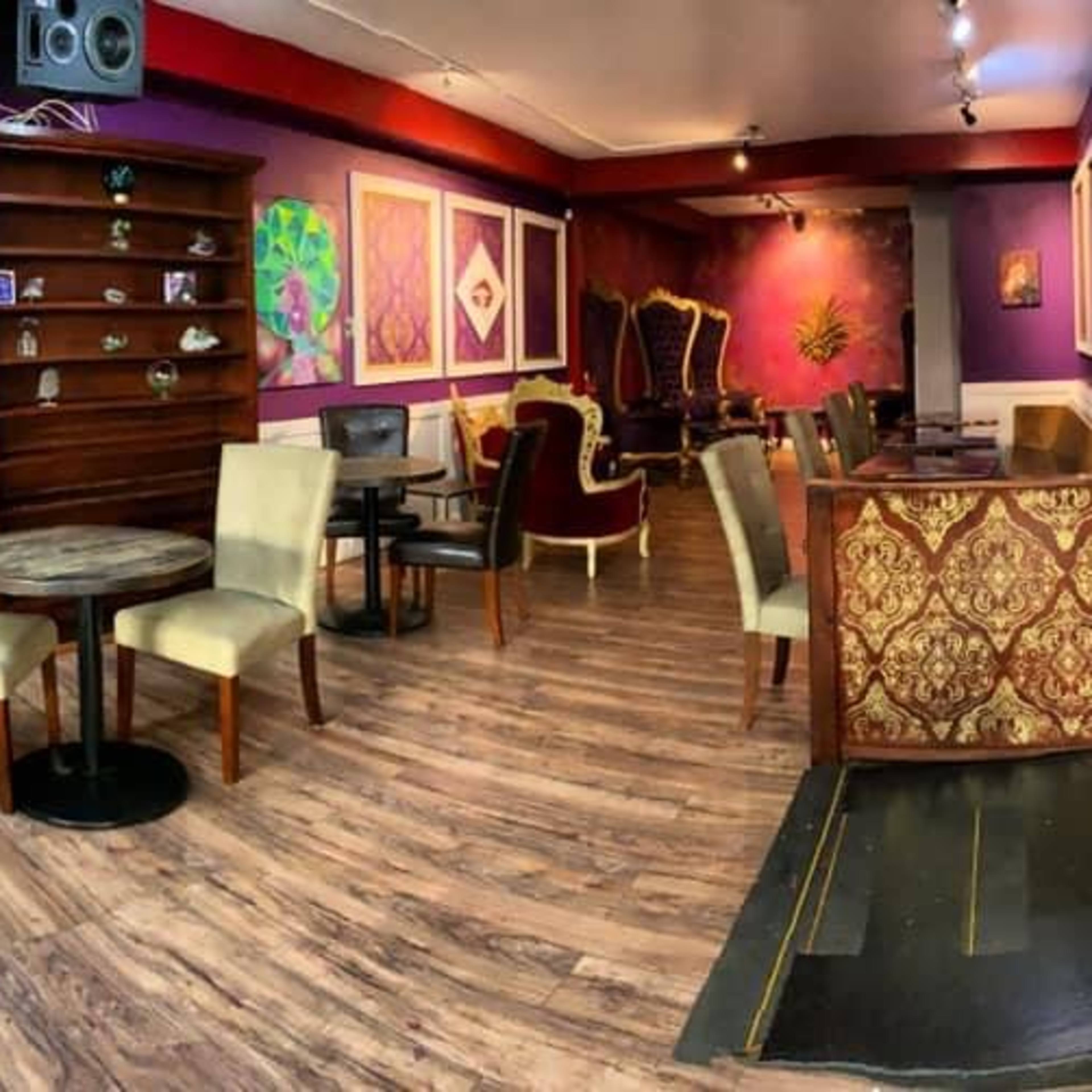 A cozy café interior with red and gold furniture, wooden shelves lined with decorative items, and a mix of seating arrangements including tables and chairs.